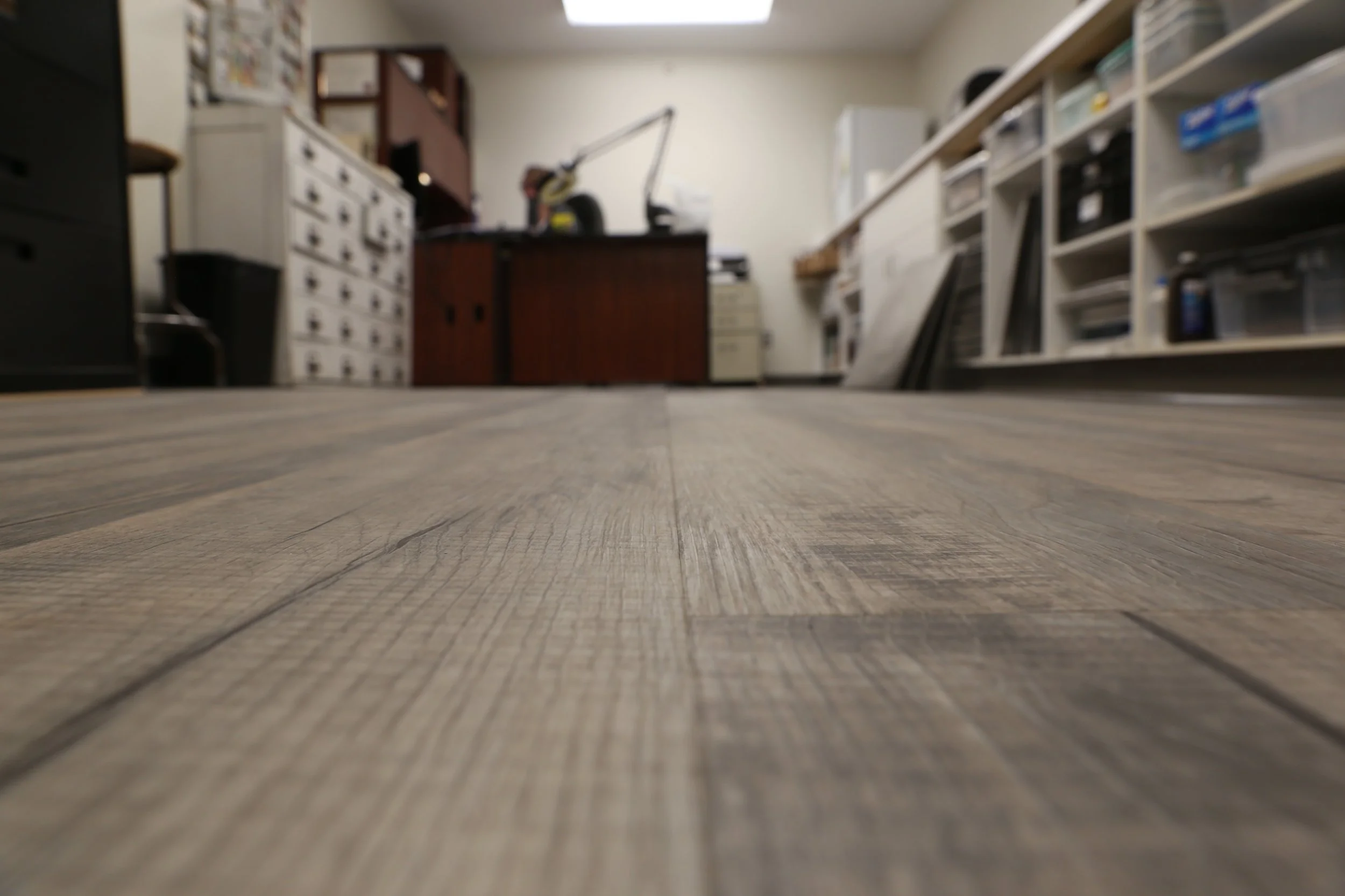 View of a woodworking or craft room with a wooden floor, workbenches, tools, and storage cabinets.