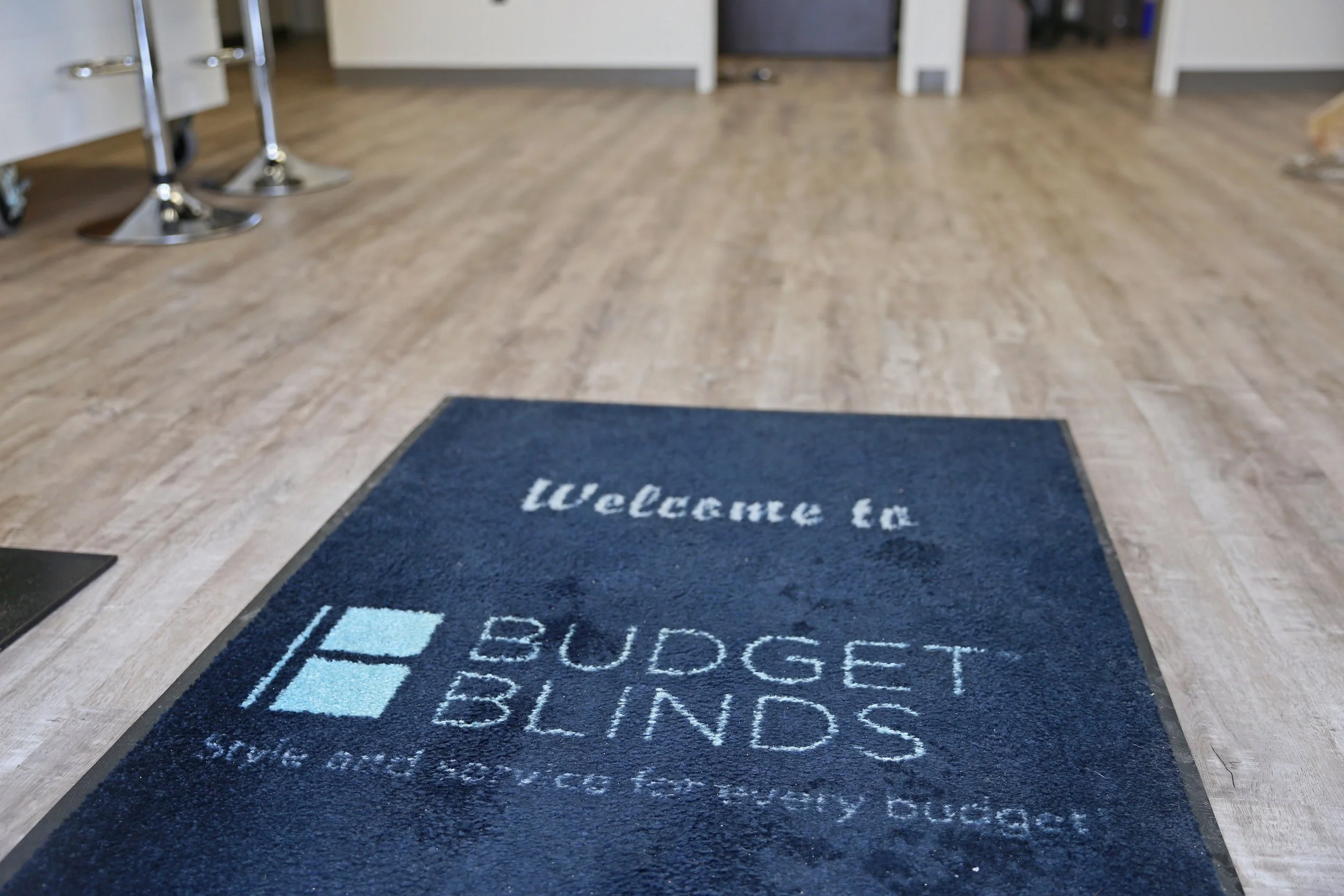 Welcome mat with the text 'Welcome to Budget Blinds. We serve with integrity and dignity.'