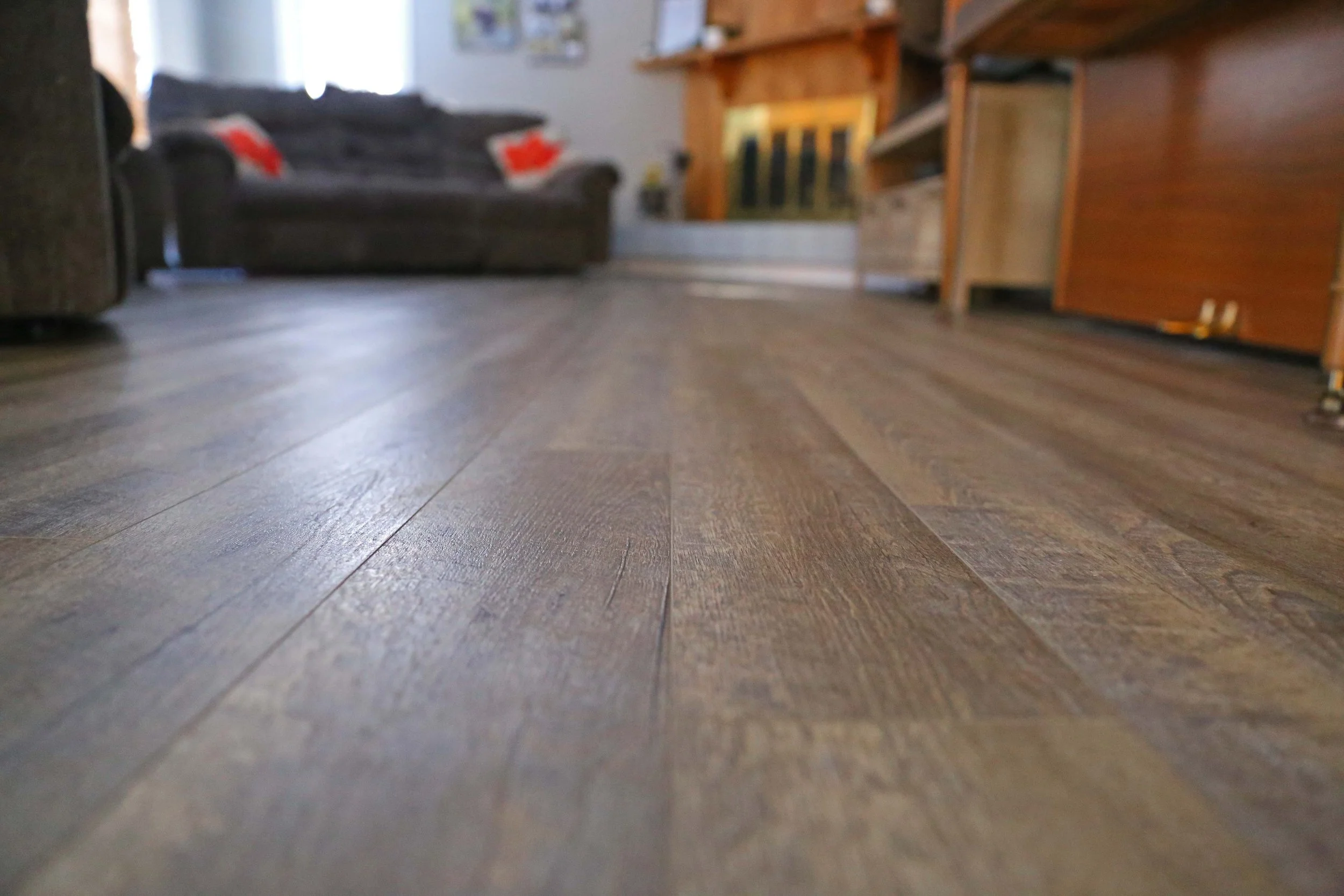 Close-up of wooden flooring in a living room with furniture and couches in the background.