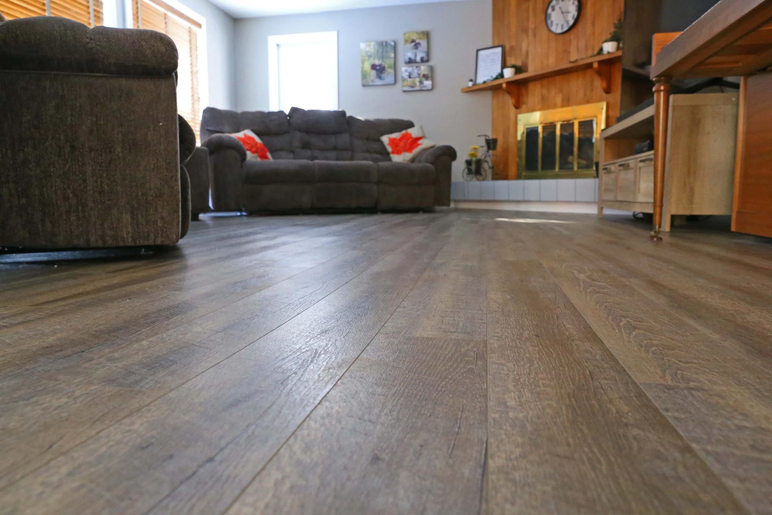 Living room with brown sofas, wooden fireplace, picture frames, clock, and wood flooring.