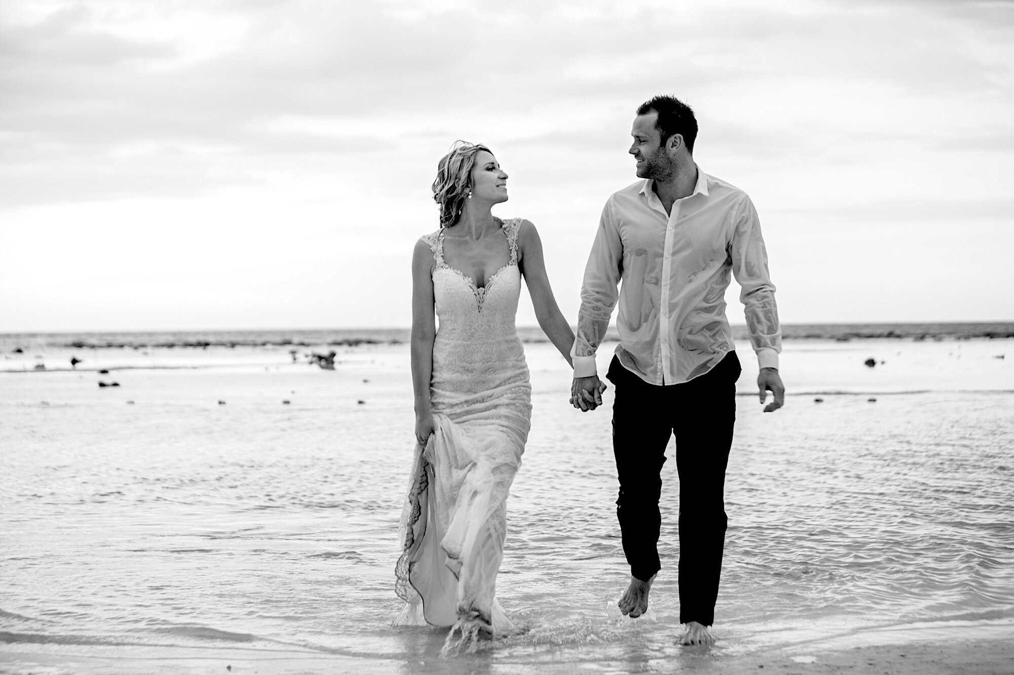 bride groom walking in shallow ocean holding hands smiling at each other black and white.jpg