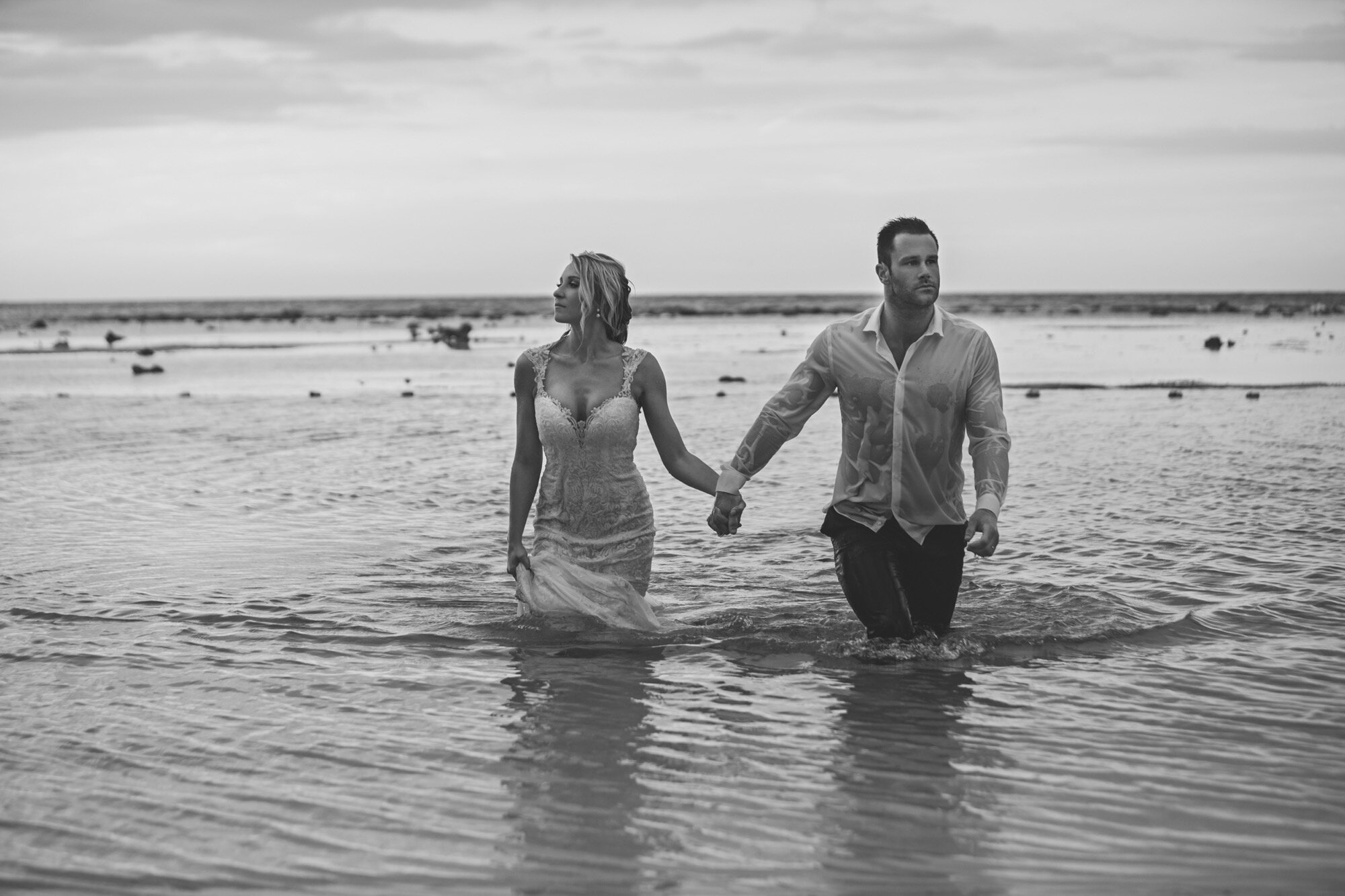 bride groom walking out of ocean holding hands editorial black white.jpg