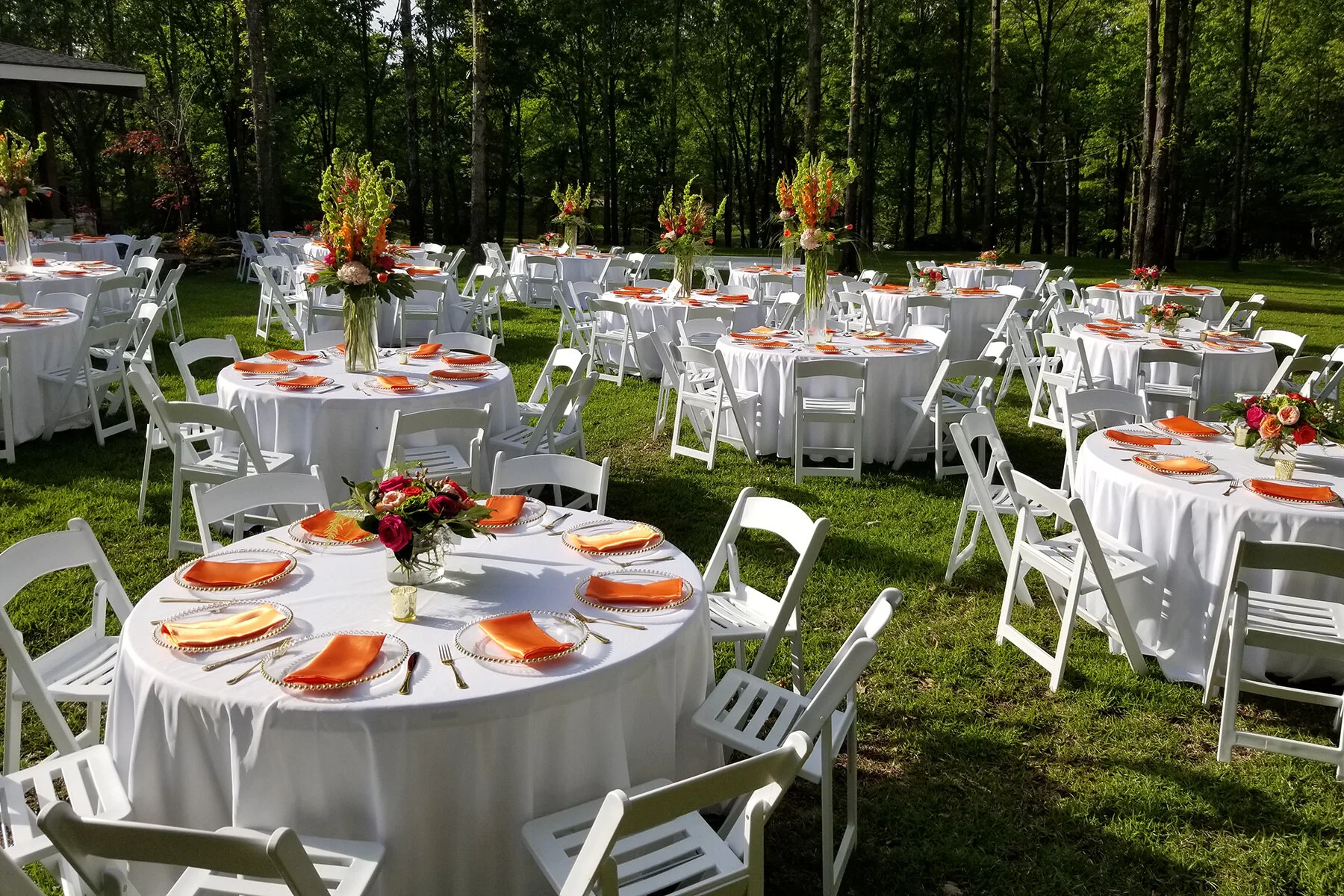 A bright sunny day covering a large outdoor space filled with round tables and white chairs and flowers to fit the occasion.