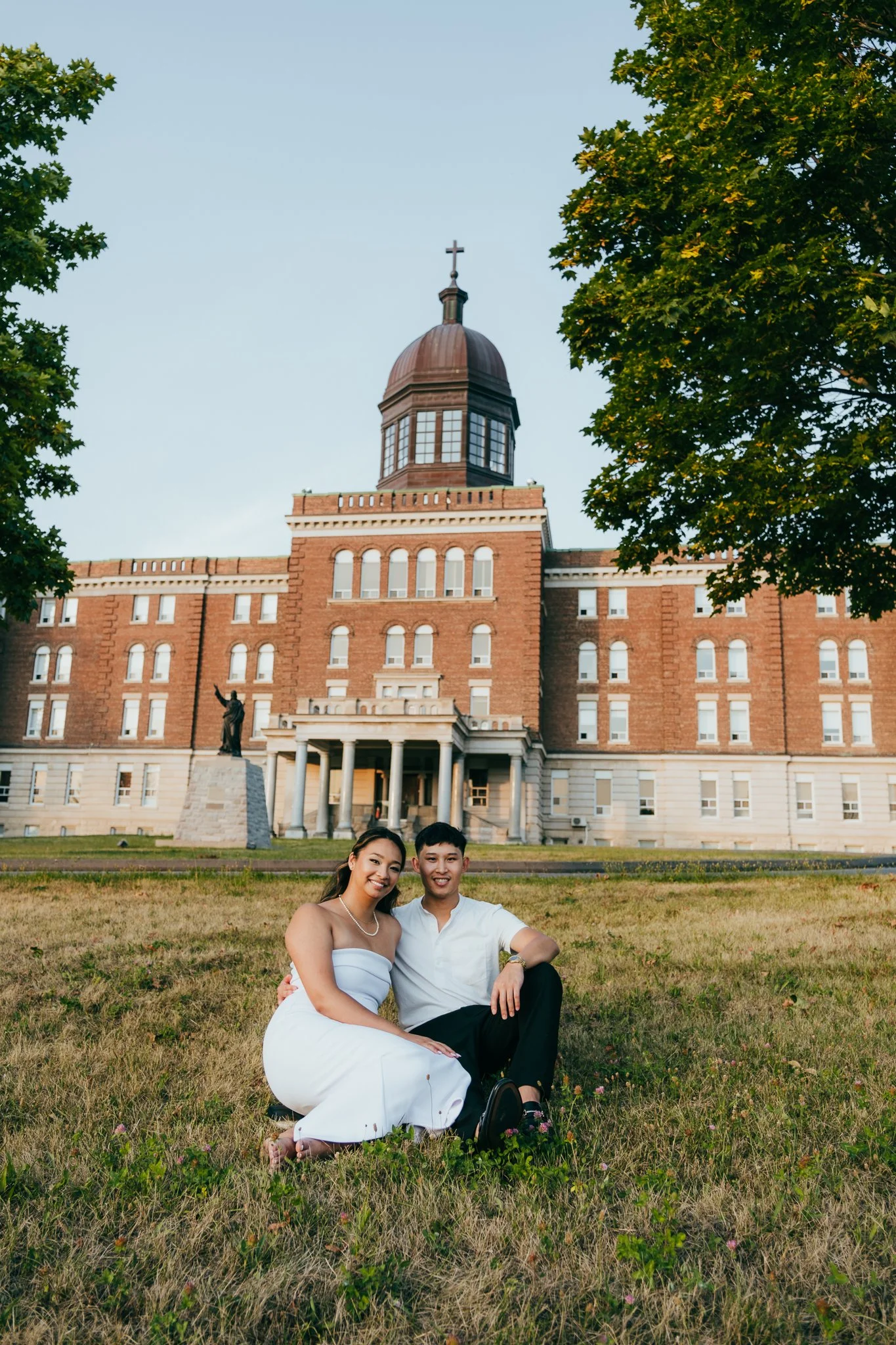 Beautiful image of couple sitting on a open green field infront of an old Catholic college in Scarborough.