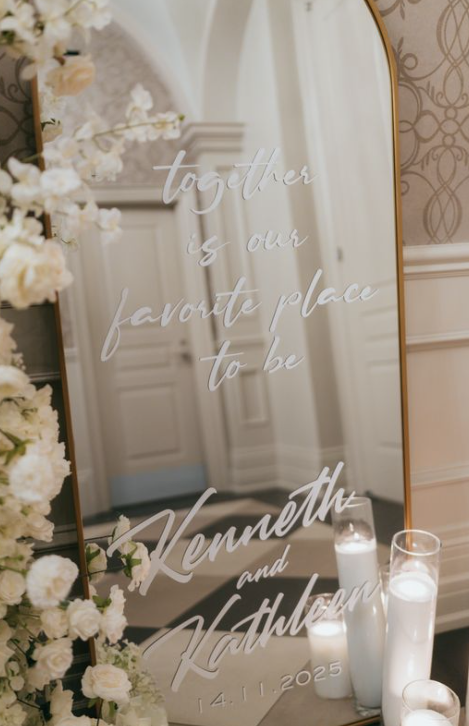 A mirror with a wedding message inscription, decorated with white flowers and candles, in an elegant room.