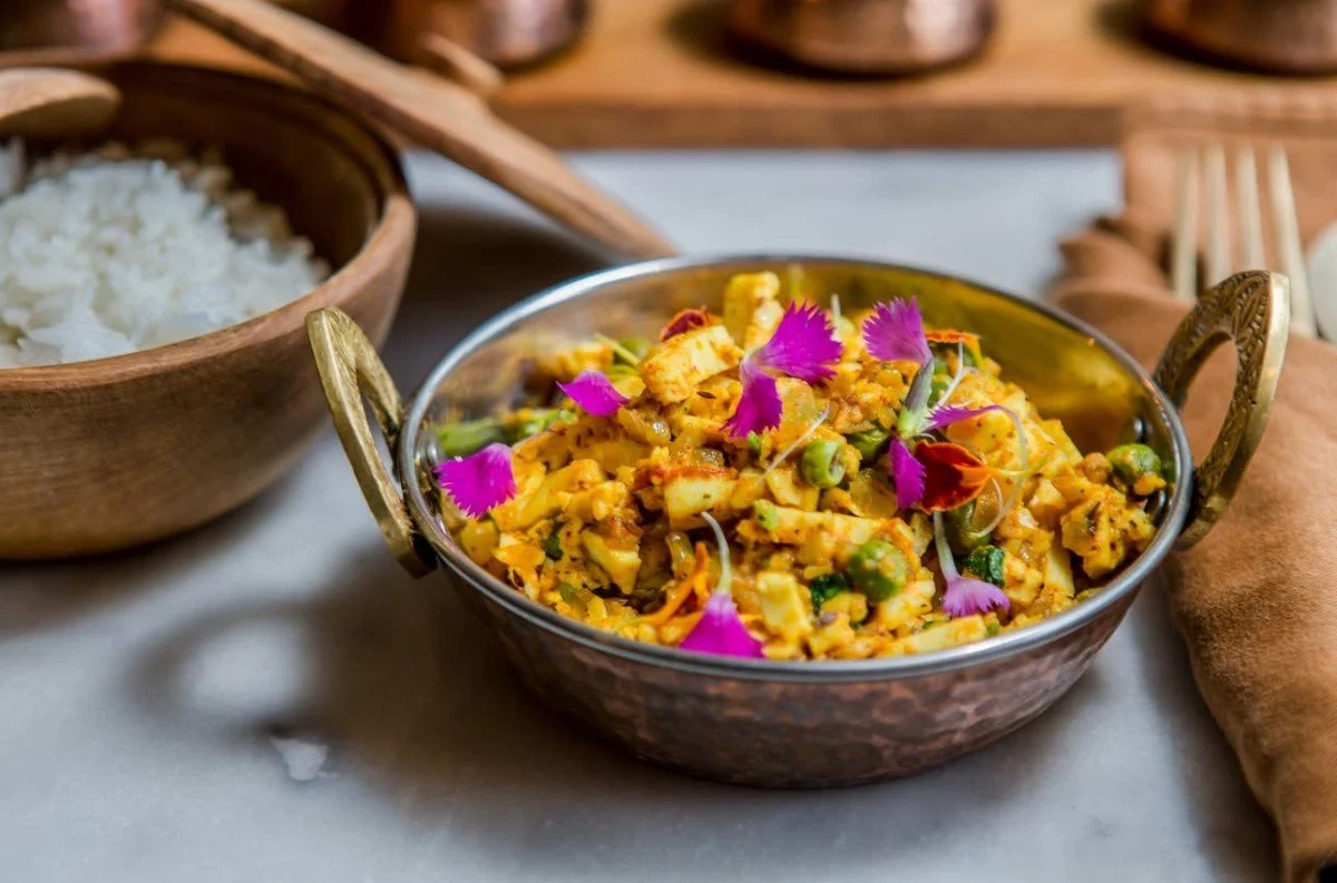 Paneer bhurji garnished with pink flower petals, served in a copper bowl beside white rice at Pesona Lounge Ubud.