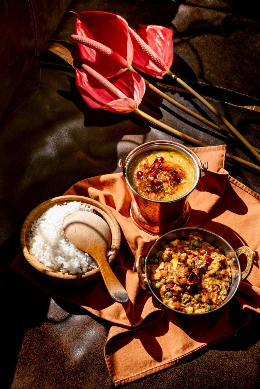 Traditional Indian curry served with steamed basmati rice and assorted house-made condiments in a copper bowl.