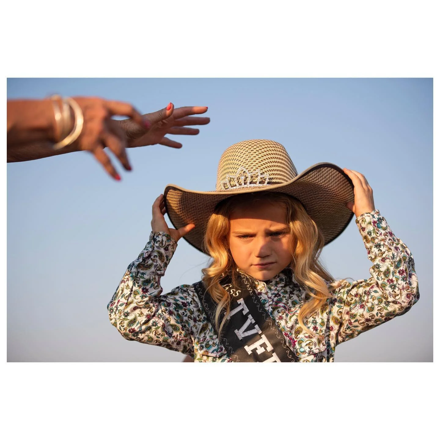 A grandmother reaches out to help her granddaughter adjust her hat at the Driggs rodeo 🌞