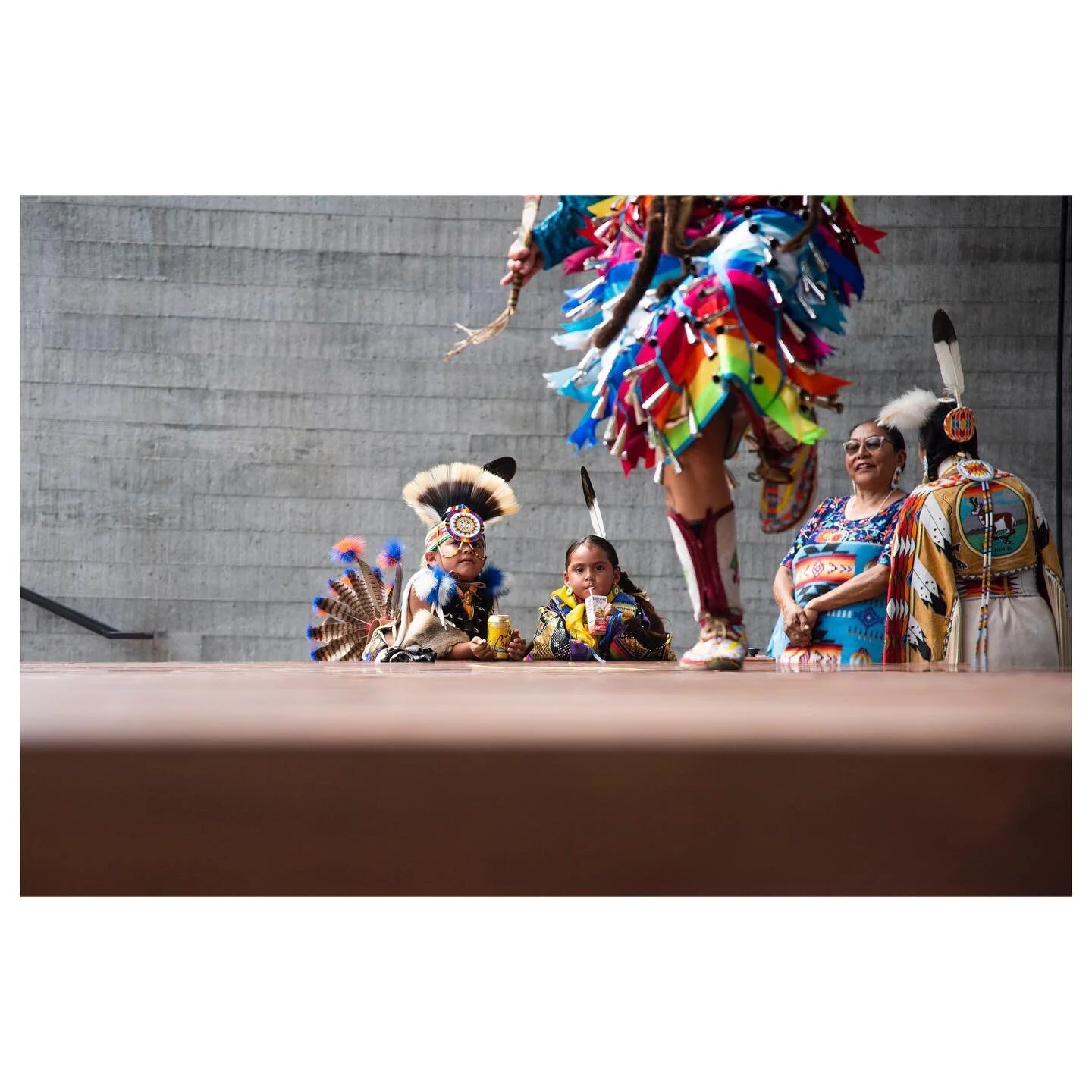 Tate Degwahnee Johnson and Cedar Lonelodge sip on a La Croix and juice box while watching Nakoosa Moreland performing a Jingle Dance on stage at the Center of the Arts.