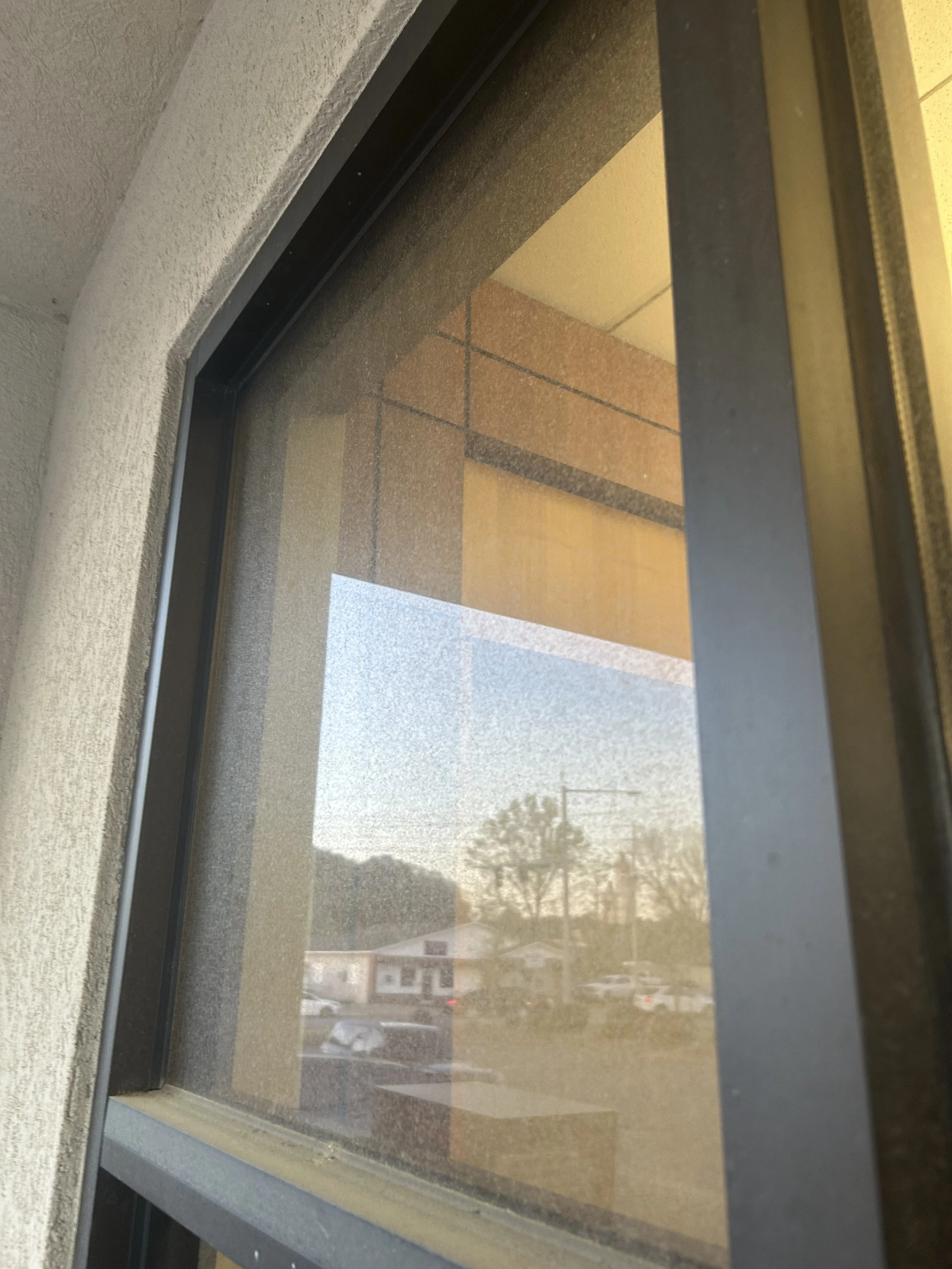 Close-up of a window with a view of a parking lot and buildings outside on a sunny day.