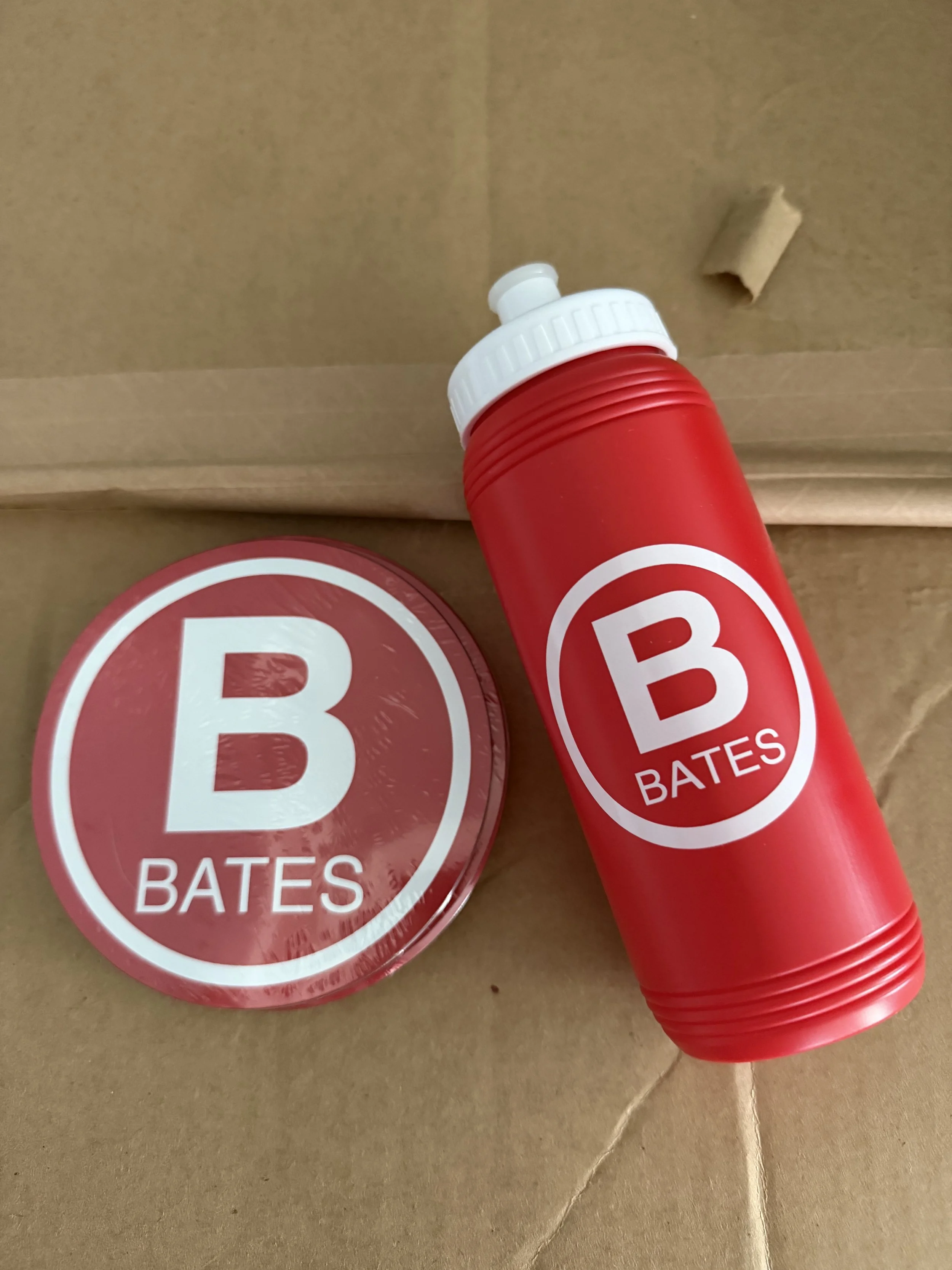 A stack of red disposable cups with the Bates logo, a red circular sticker with a white 'B' and the words 'BATES' are shown in the image.