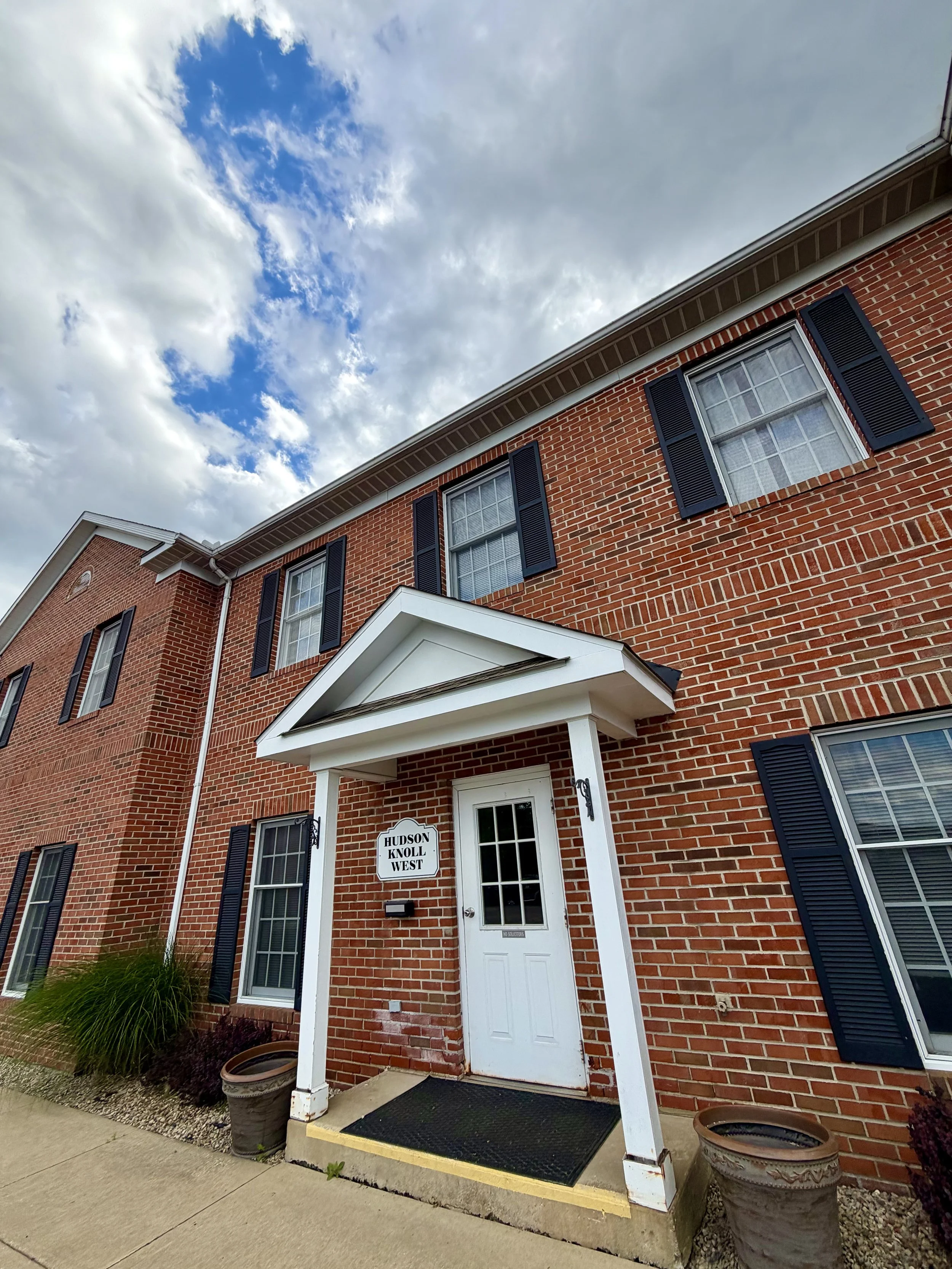 A brick office building beneath a blue sky with clouds, and a sign that says Hudson Knoll West