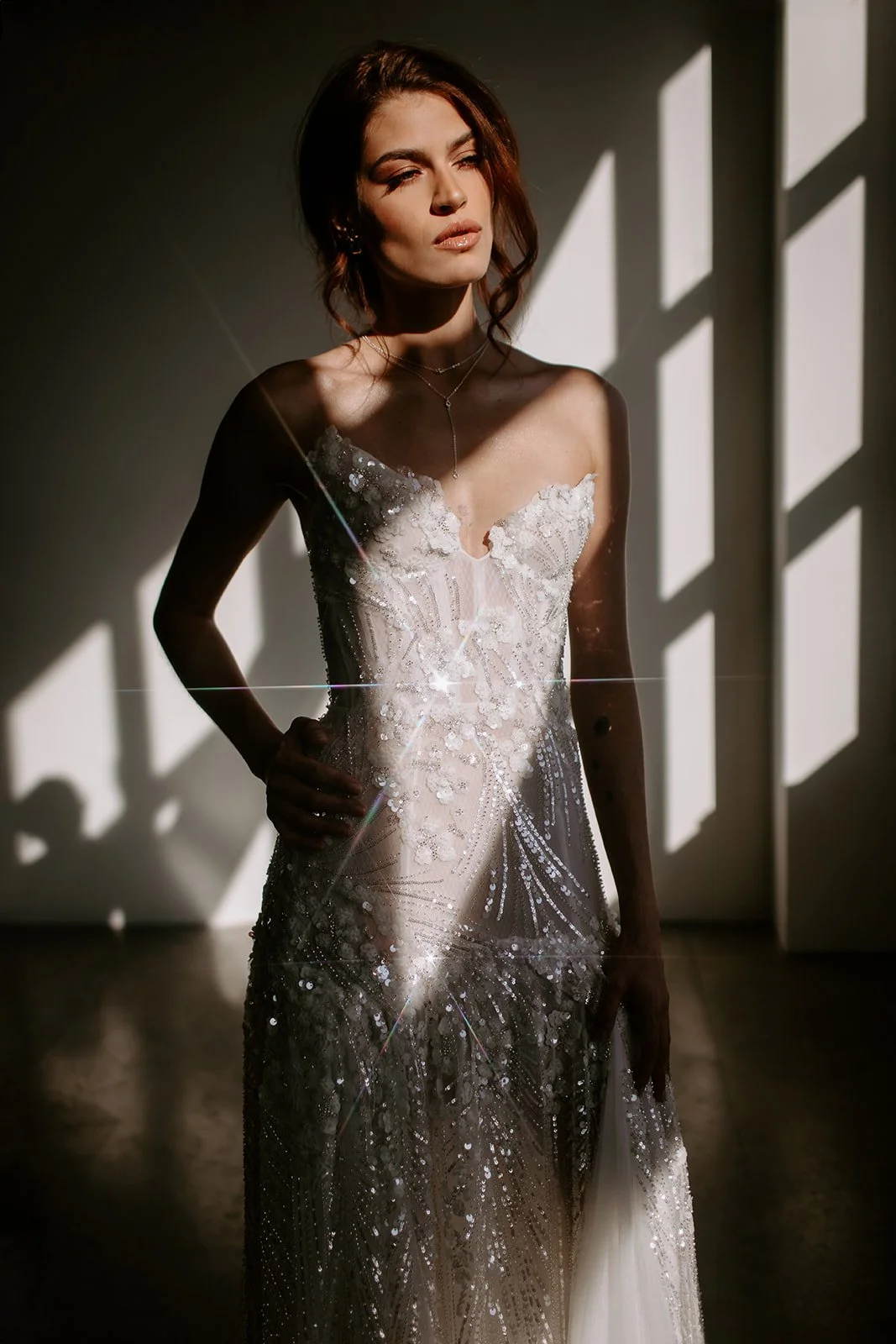 Model wearing an elegant, beaded wedding dress in a sunlit room.