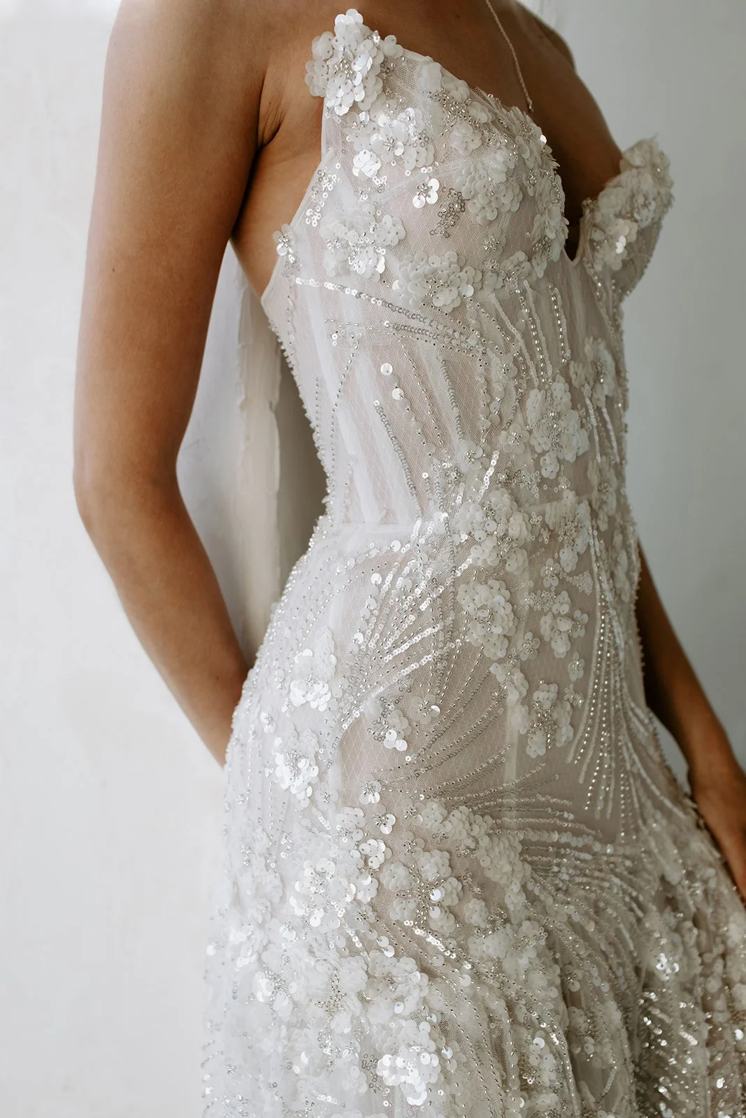 Close-up of a woman in an elegant, embellished wedding dress with floral lace and sequin details.