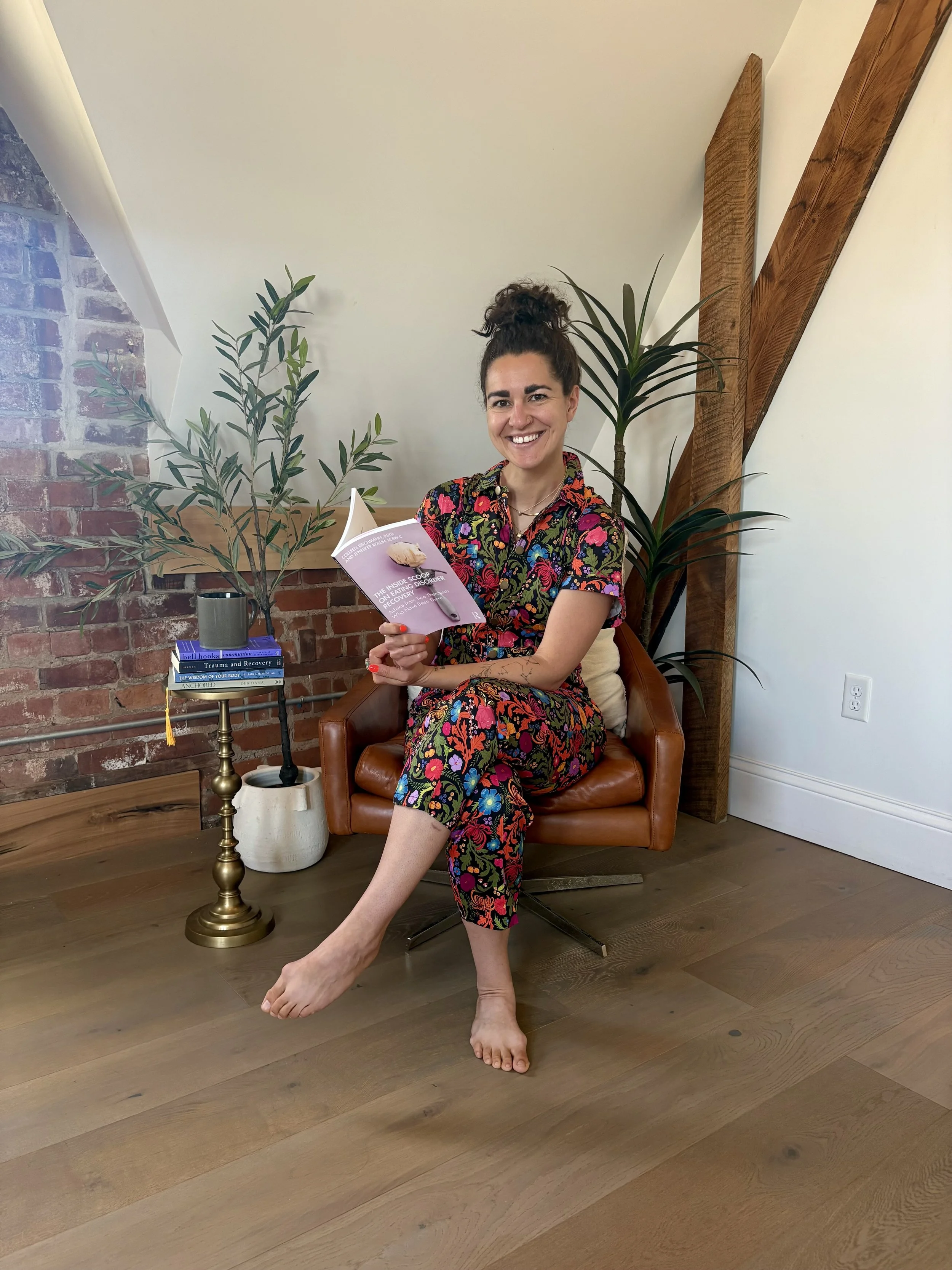 jen reading a book sitting in a leather chair surrounded by plants