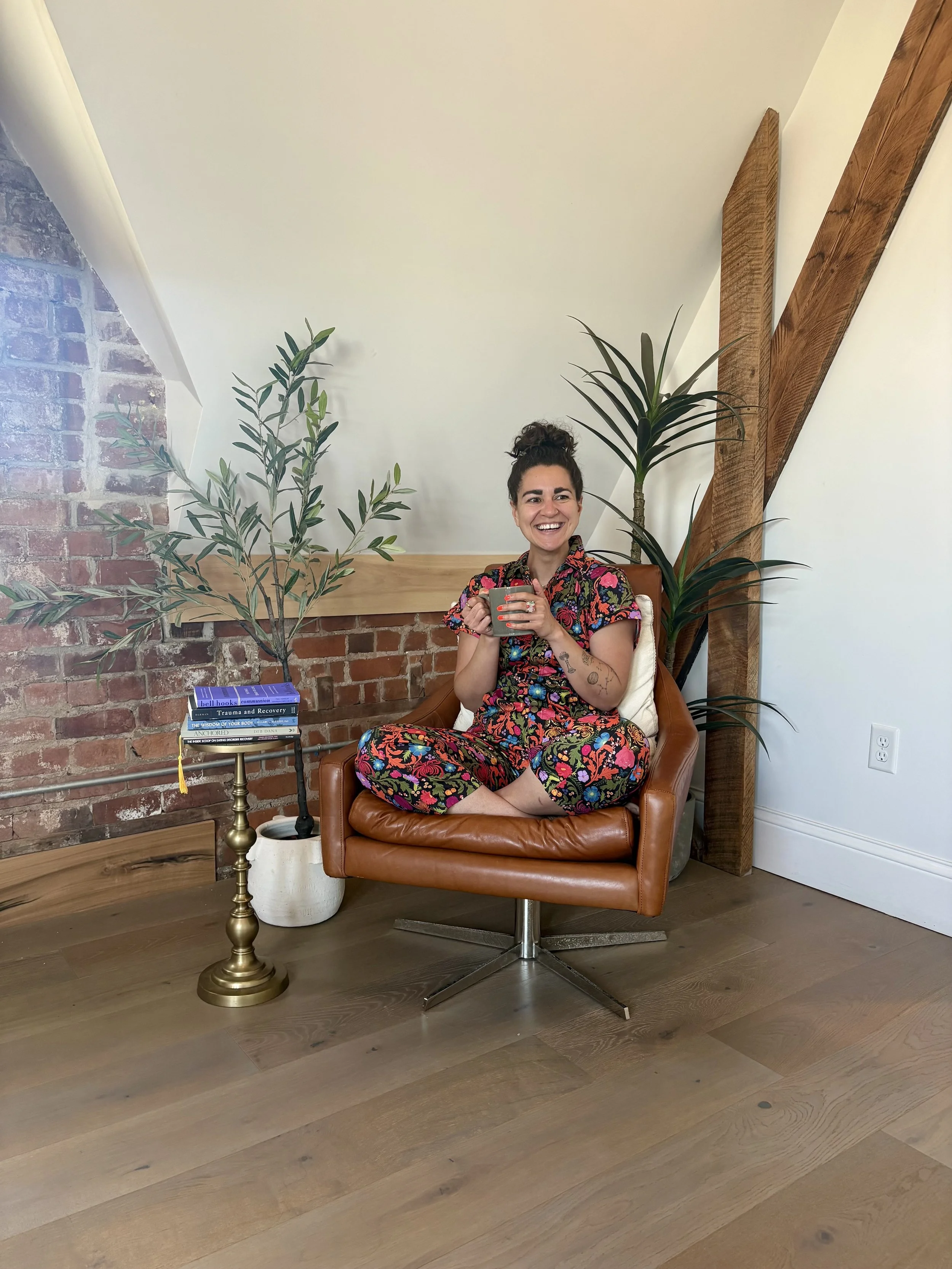 jen sitting on a leather chair holding coffee cup surrounded by plants and books