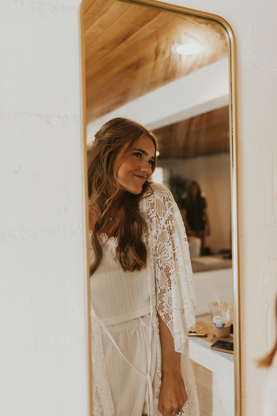 Woman in white lace dress looking in a mirror, smiling.