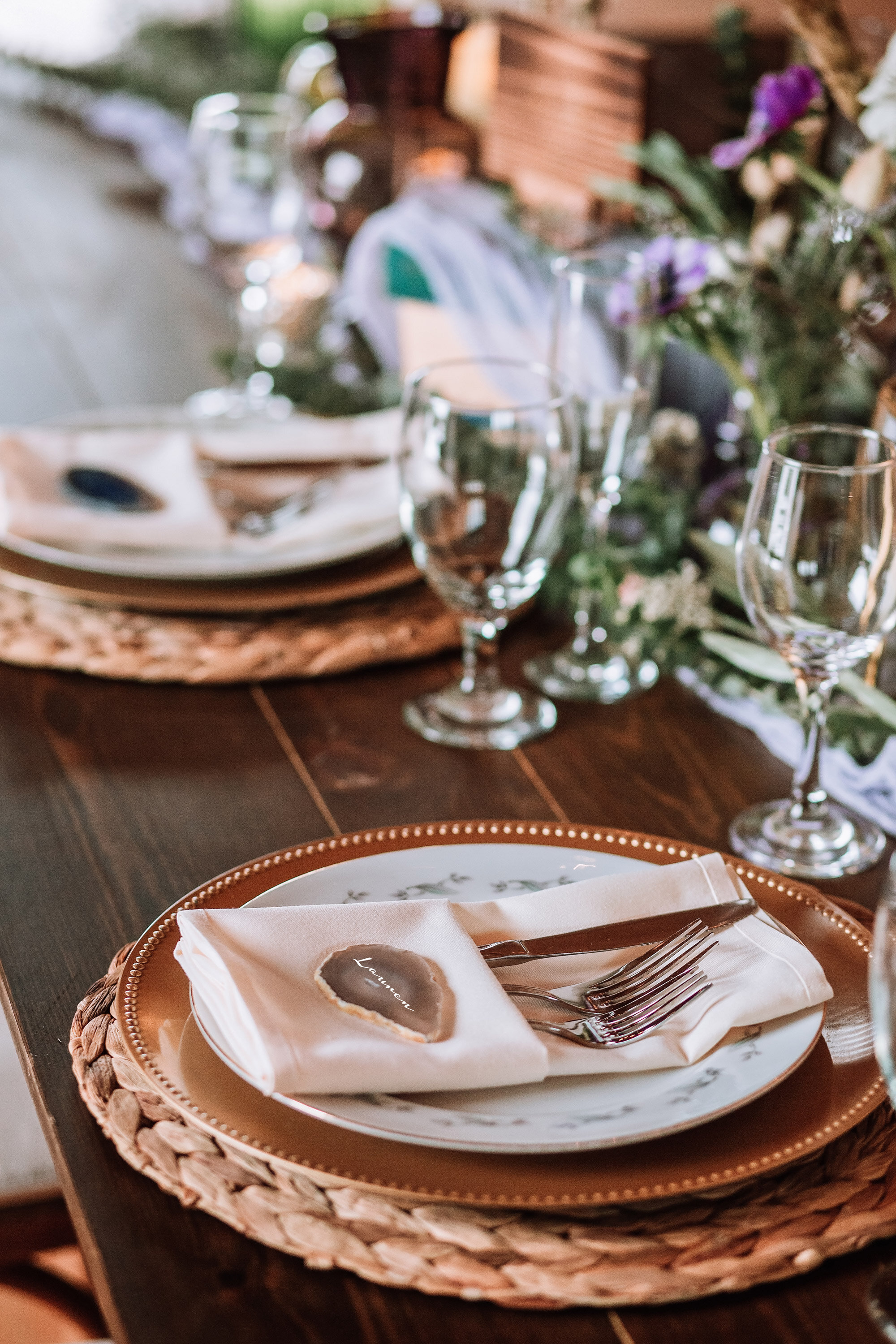 Elegant table setting with plates, napkin, cutlery, and wine glasses on a wooden table.
