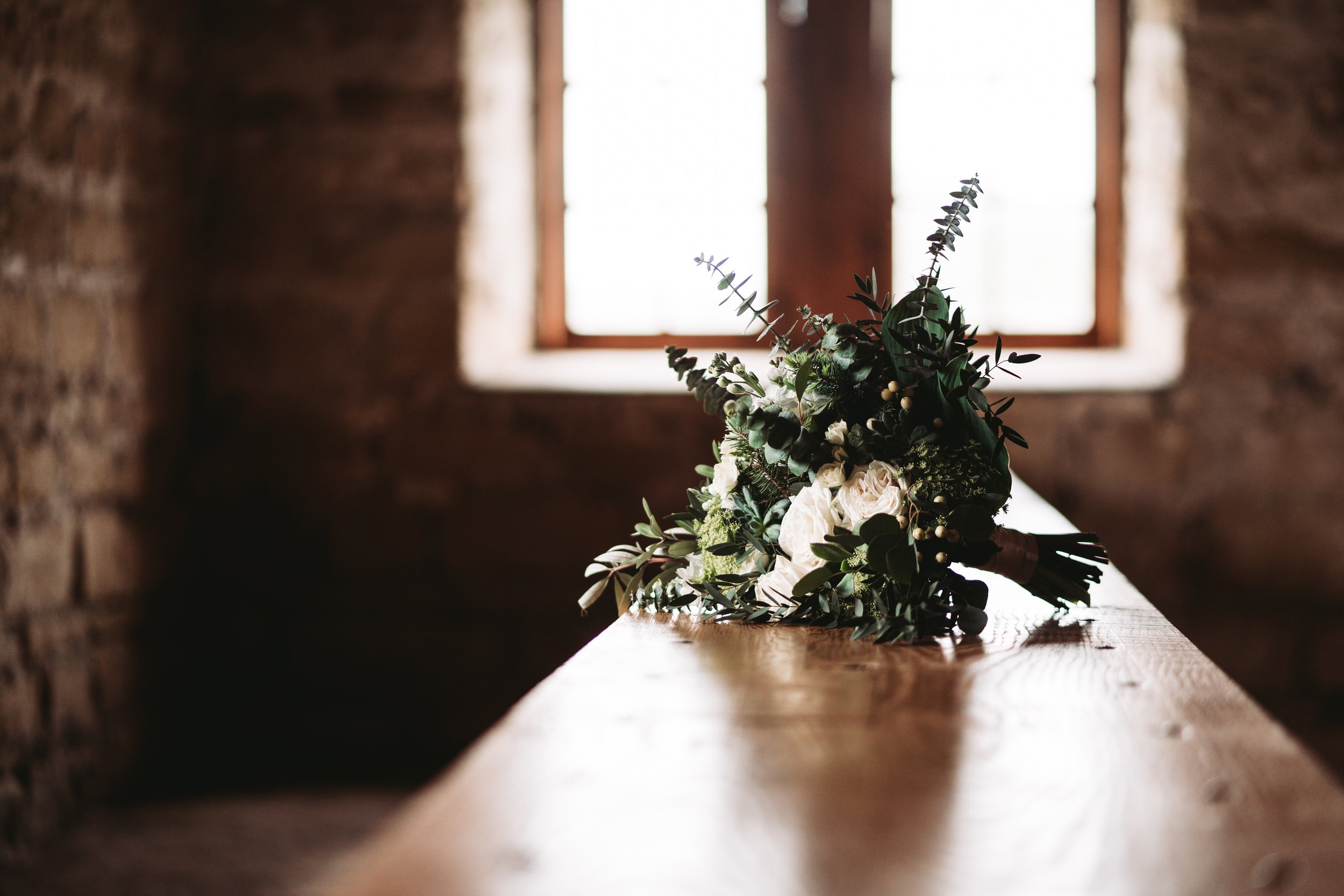 Bouquet of flowers on a wooden table with a stone wall and window in the background.