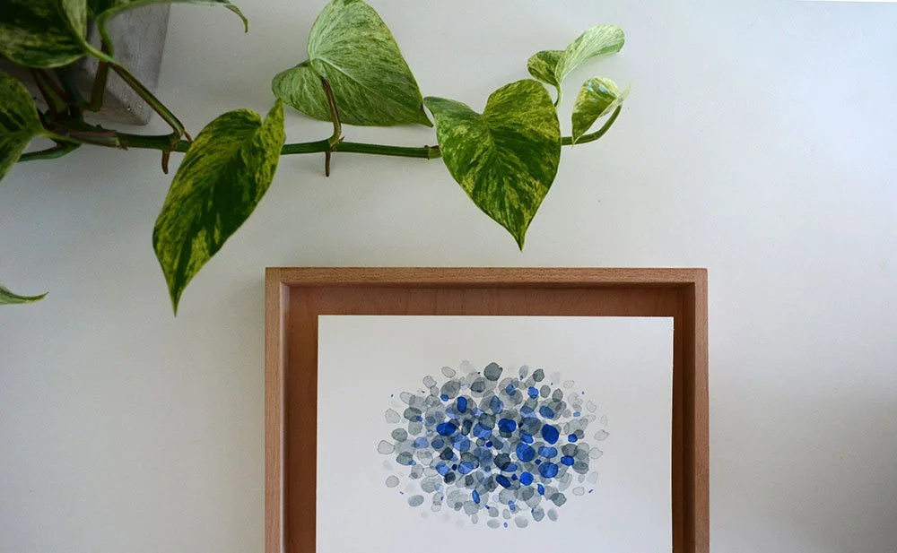 Abstract painting with blue and gray dots on a wooden frame, adorned with green pothos plant hanging above.