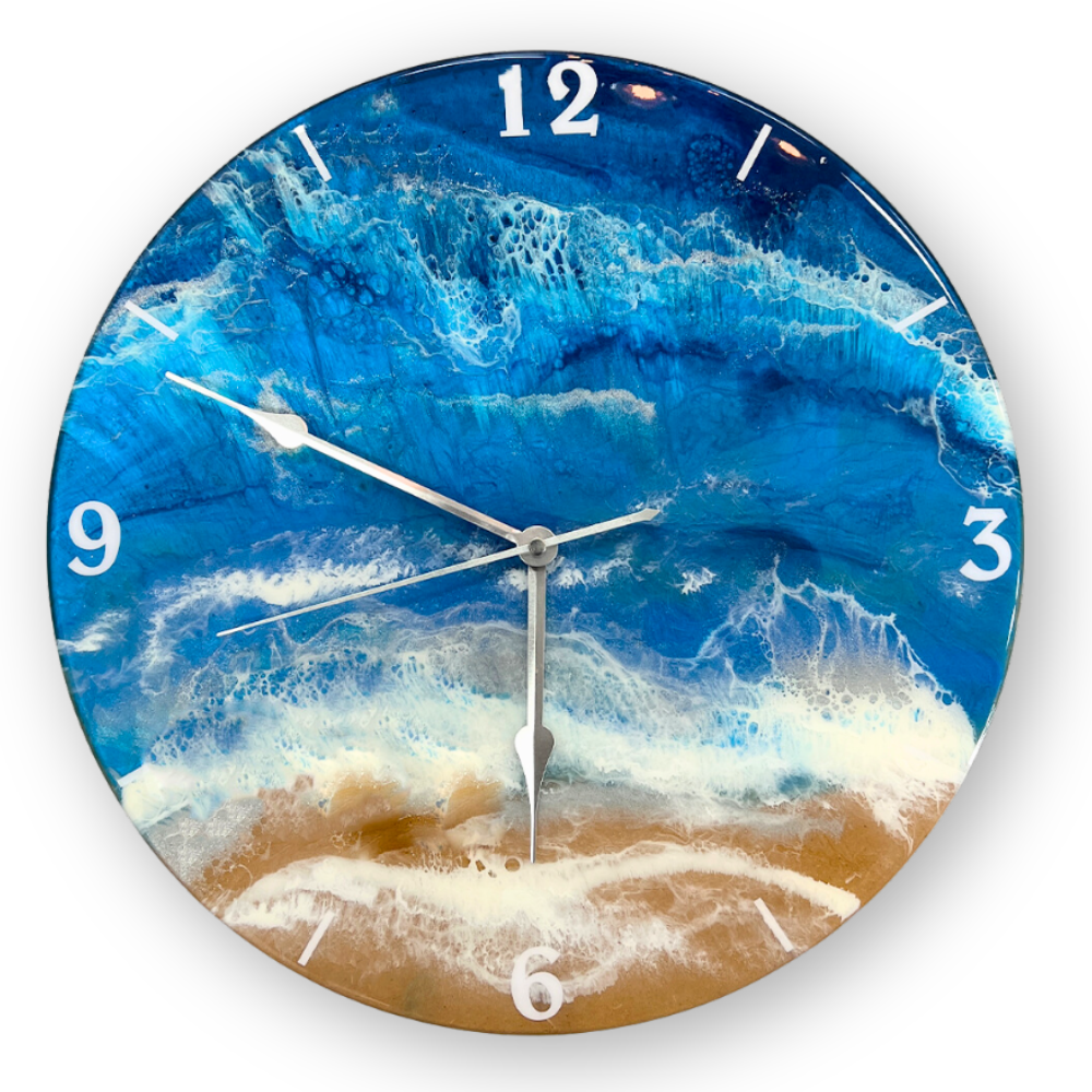 A wall clock with a ocean wave and beach scene design, featuring blue water, white foam, and sandy shore, and white hour markers.