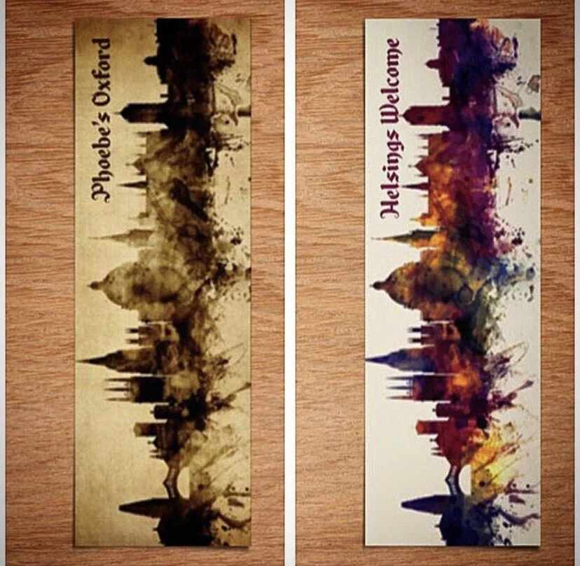 Two bookmarks with watercolor cityscape silhouettes. The left bookmark features a sepia-toned skyline labeled 'Phoebe's Oxford.' The right bookmark features a colorful cityscape labeled 'Helsingin Welcome,' with vibrant hues and a white background.