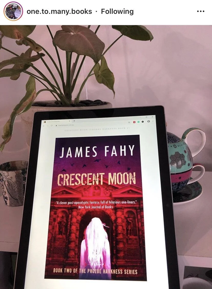 A digital tablet displaying the book cover of 'Crescent Moon' by James Fahy. The cover shows a woman with long white hair facing a building with arches and a glowing red sky with flying birds. There is a potted plant with green leaves behind the tabl
