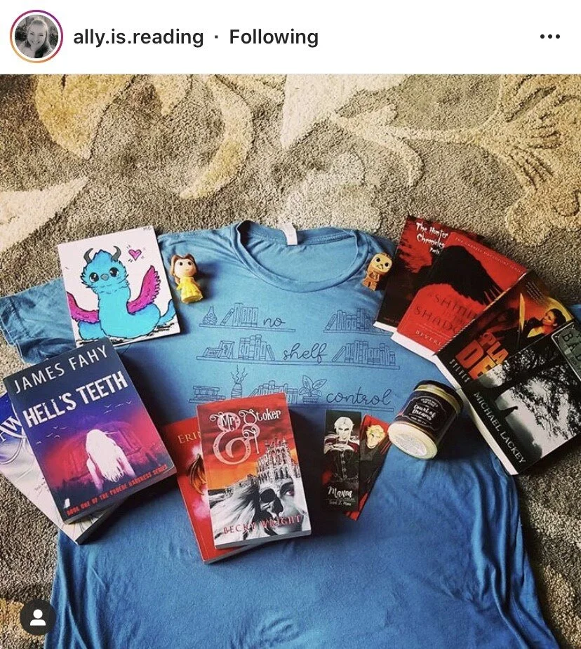 A blue T-shirt with the text 'no shelf I control' surrounded by books, a sketch of a shelf, a picture of a dragon, several small toys, and books including 'Hell's Teeth,' 'The Monster Chronicles,' and 'Shadow of the Demon.'
