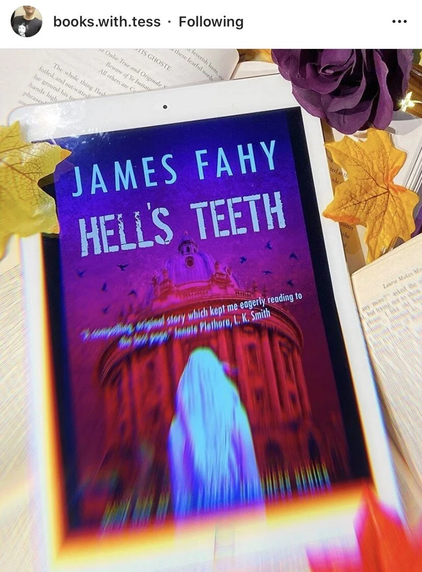 A digital device displaying the book cover of "Hell's Teeth" by James Fahy, with a background of open books, purple flowers, and autumn leaves.