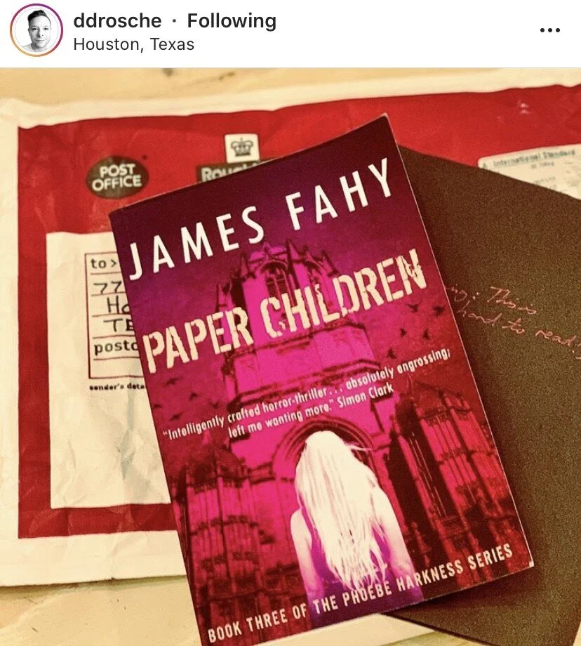 A copy of the book "Paper Children" by James Fahy on top of an envelope with postage labels and a border collie dog to the right. The book is part of the Phoebe Harkness series.