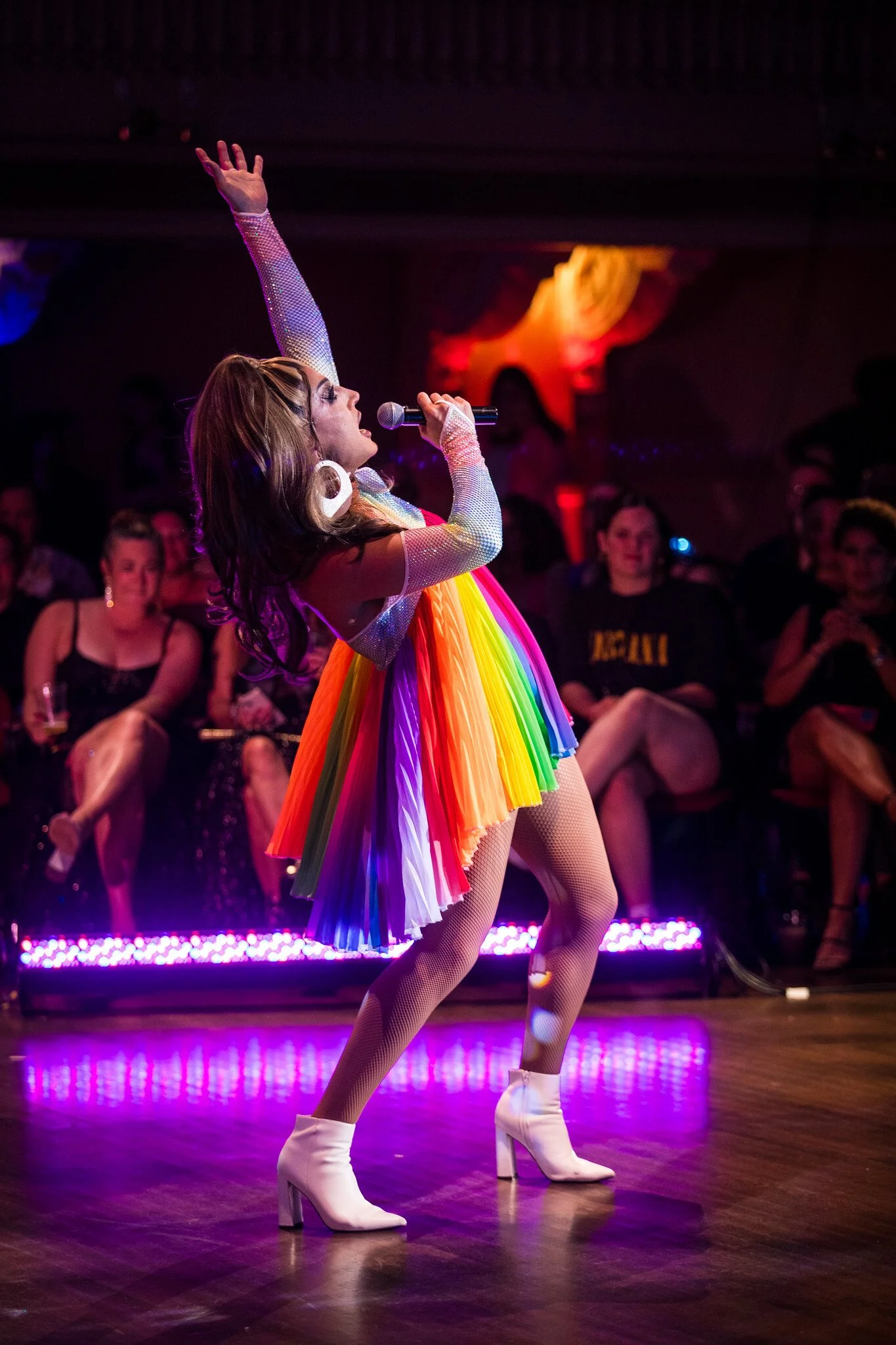 Jackie Cox in drag on stage at the Queer AF in a rainbow outfit.