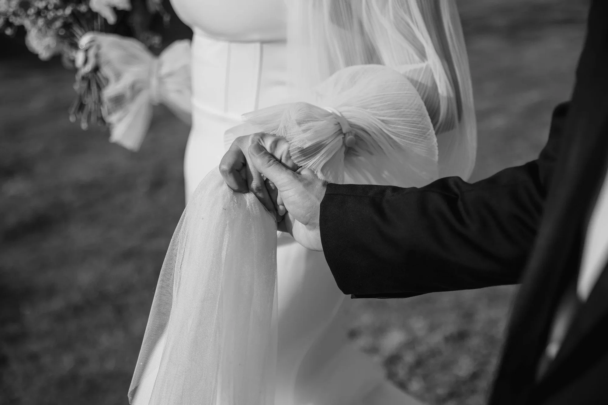A bride and groom holding hands during a wedding ceremony, with the bride wearing a veil and gown, and the groom in a dark suit. The photo is in black and white. Suffolk Wedding Photographer / Essex Wedding Photographer
