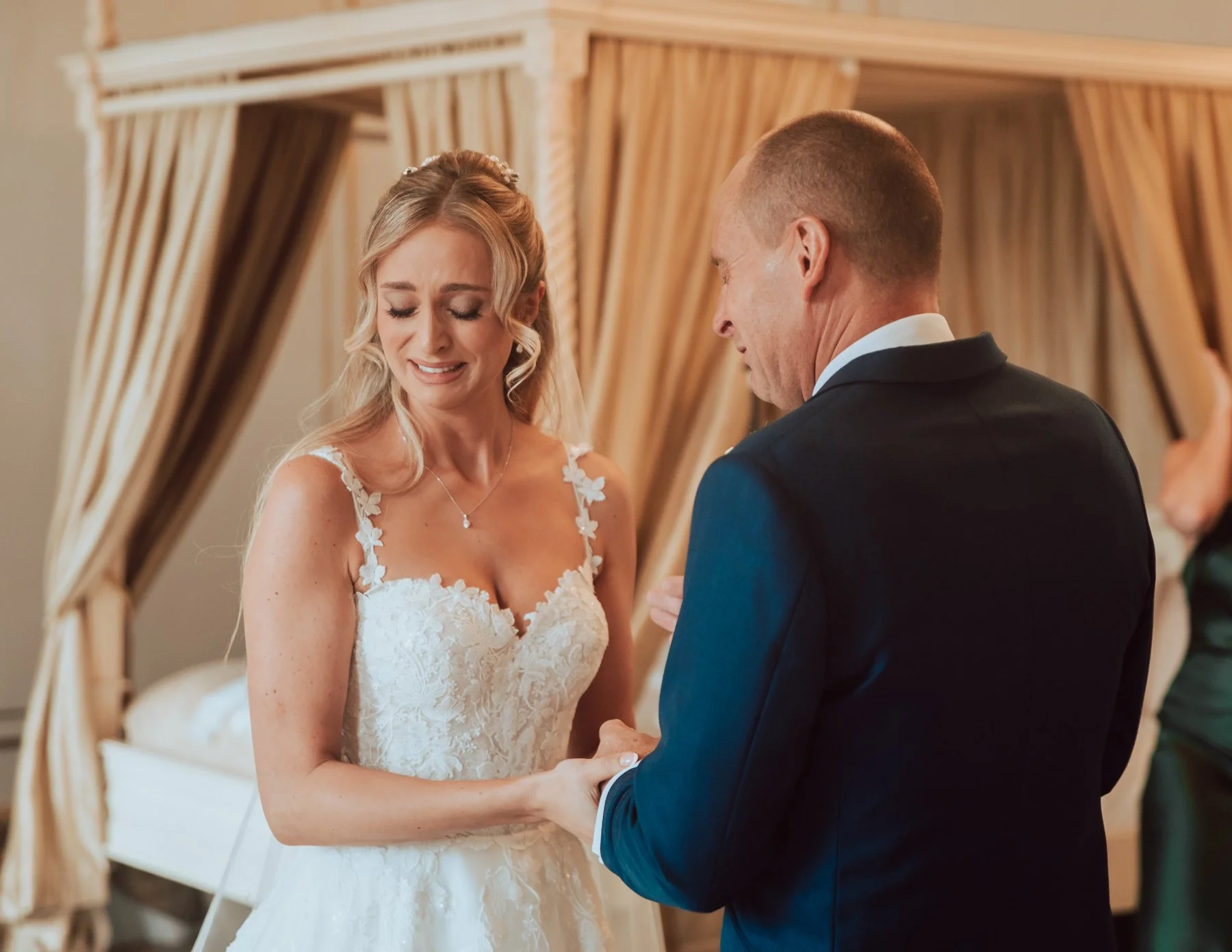 Bride in lace wedding dress holding hands with man in suit, emotional moment indoors. Captured by Luxury Essex Wedding Photographer Liam Gillan Gosfield Hall Essex