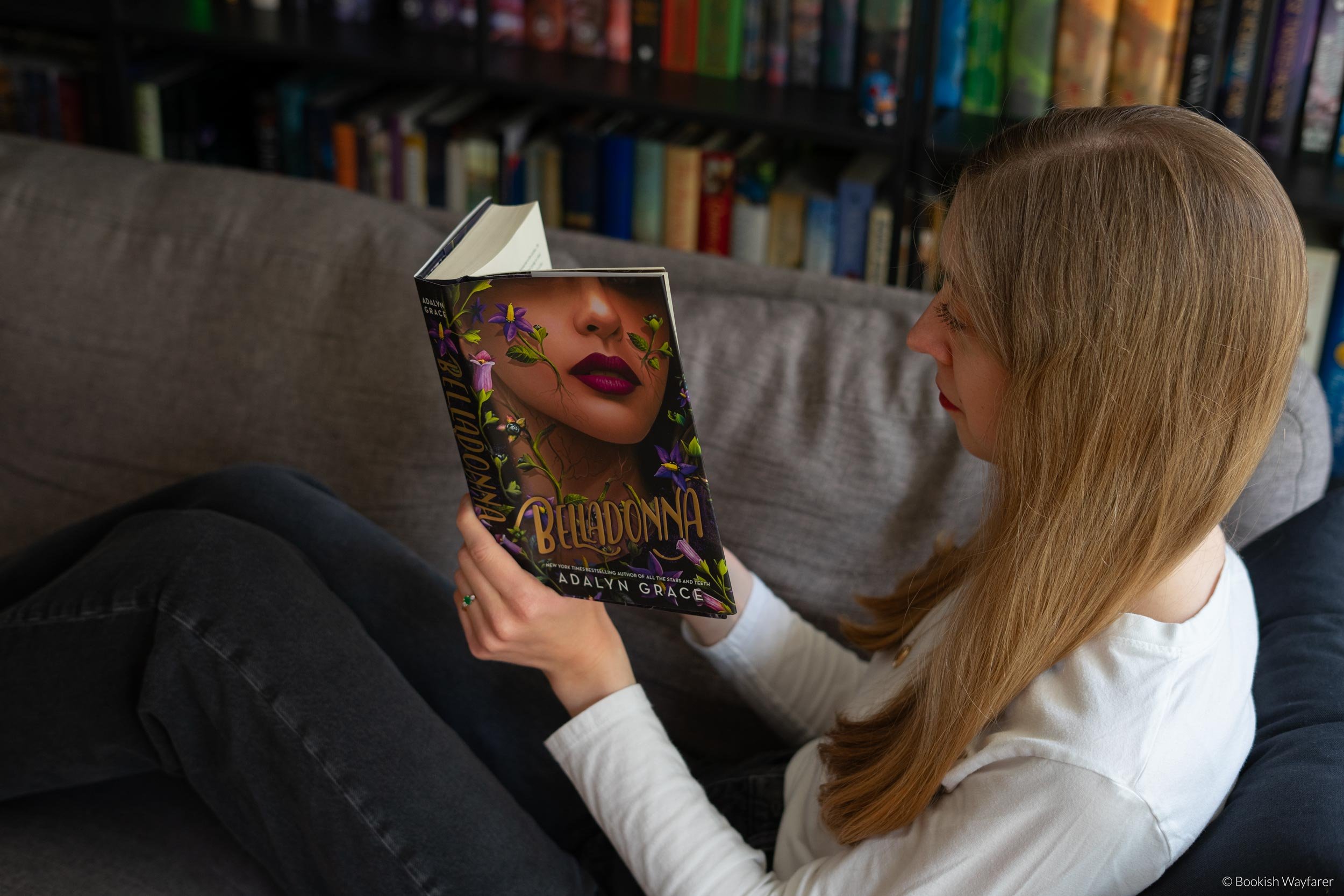 A woman sits on a sofa reading the book Belladonna