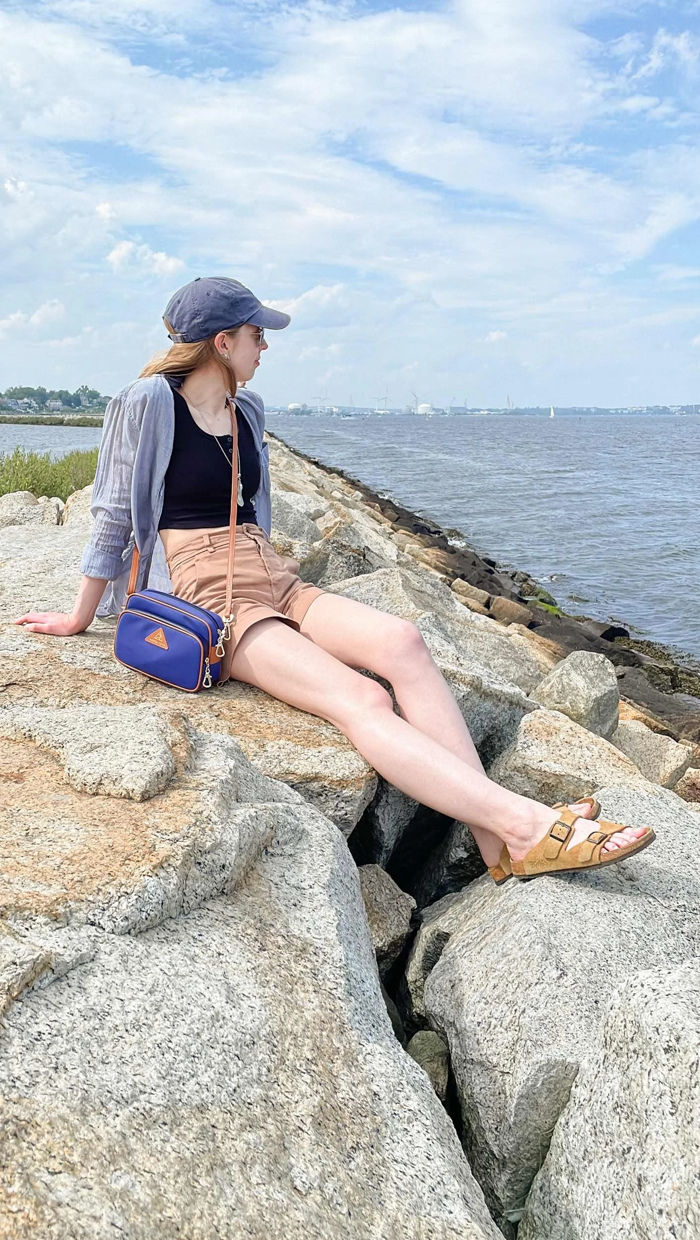 The author, Julia, poses along a rocky coastline with Arden Cove's Crissy Full Crossbody Purse