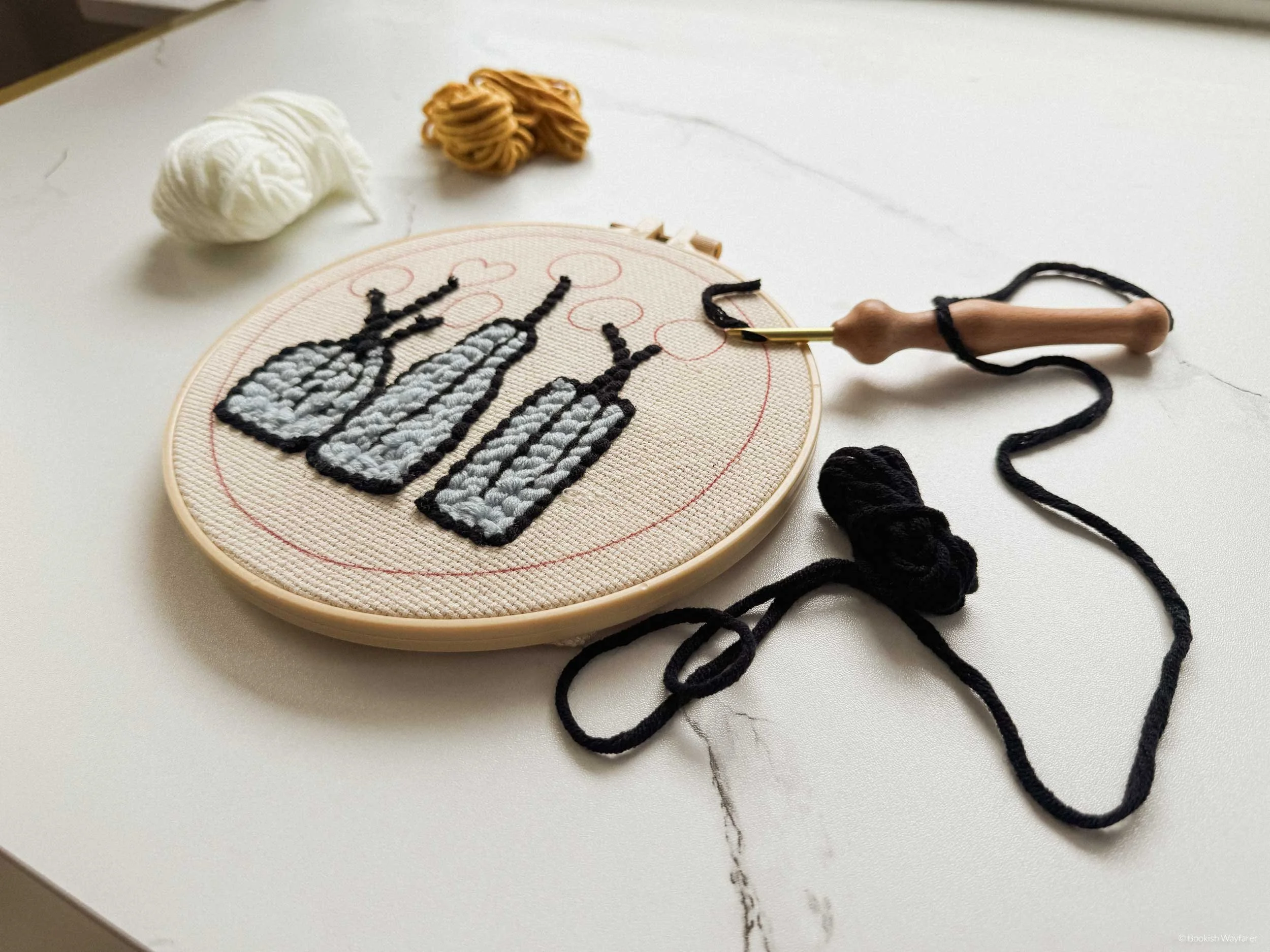 A partially completed punch needle design laid flat atop a table with balls of yarn