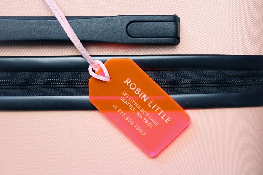 A transparent, orange luggage tag with the name Robin Little engraved into it