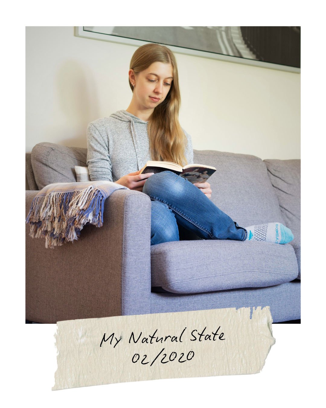 The author sitting on a grey sofa with a book in hand
