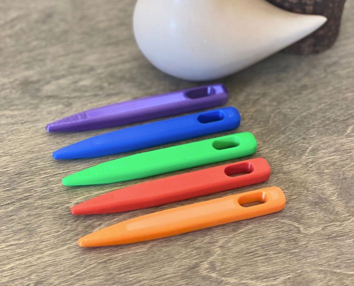 5 toothbrush rug needles of various colors laid flat atop a wooden table