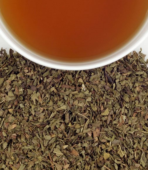 Loose-leaf peppermint tea in front of a cup of peppermint tea