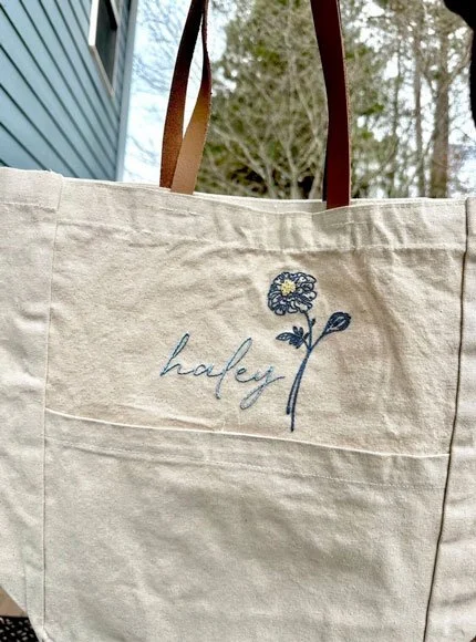 A tote bag with the name Haley and a blue flower embroidered on it