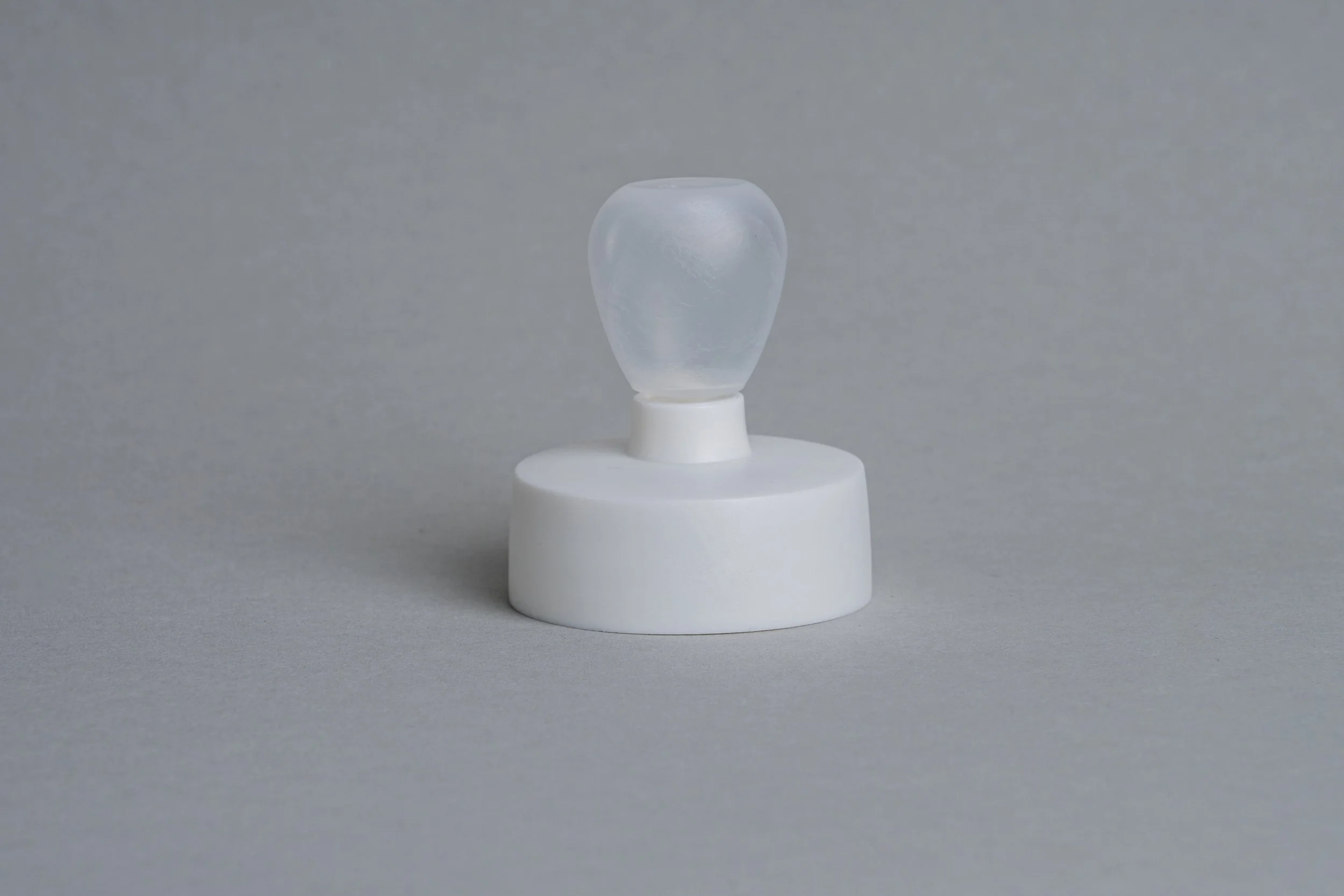 A translucent white ice cube on a white round pedestal against a gray background.