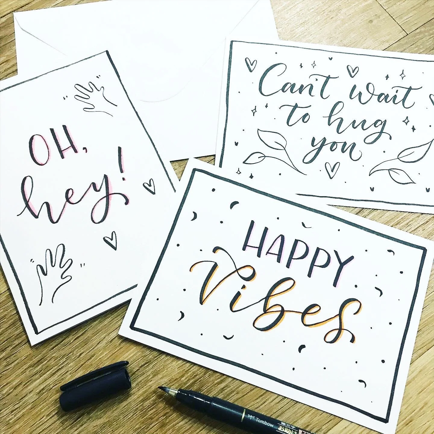 Three handwritten greeting cards with messages, surrounded by black marker and an envelope on a wooden surface.