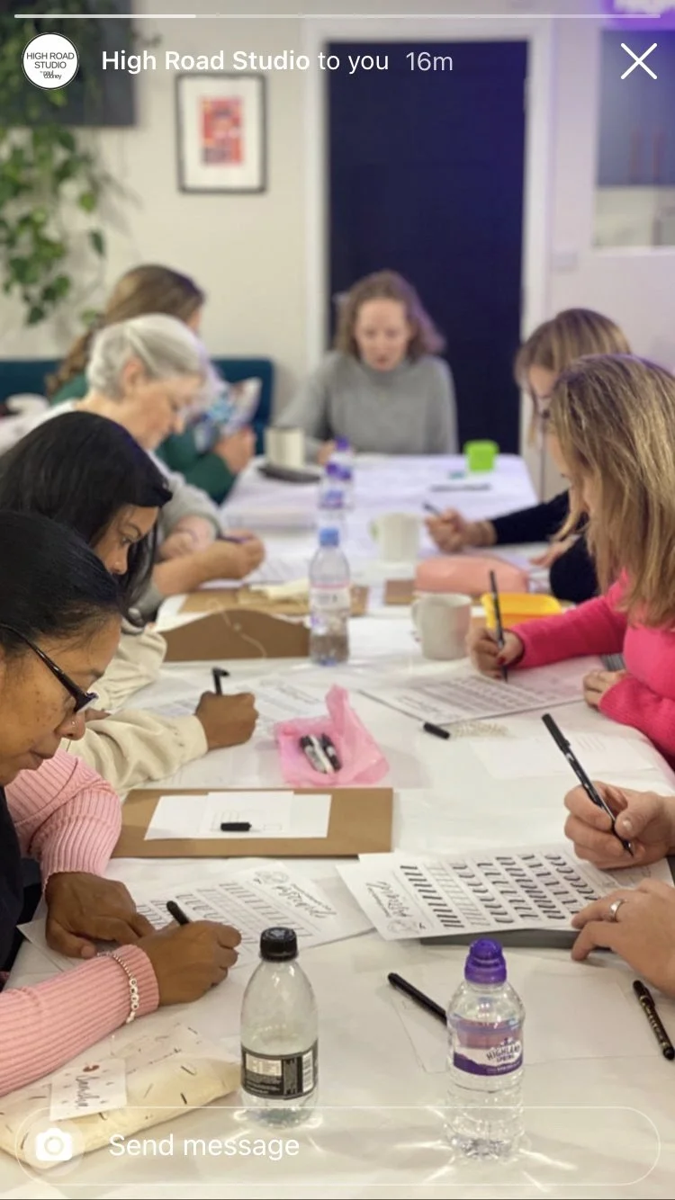 A group of women sitting around a table engaged in a craft or writing activity, with various materials and bottles of water on the table.