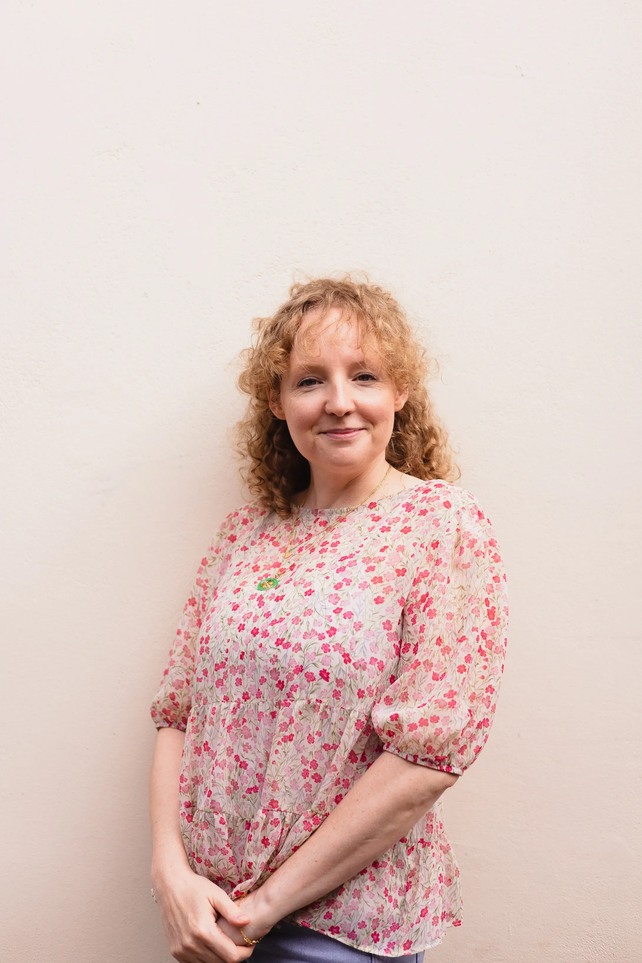 London calligraphy artist, Laura Edralin wearing a pink floral top standing against a plan background