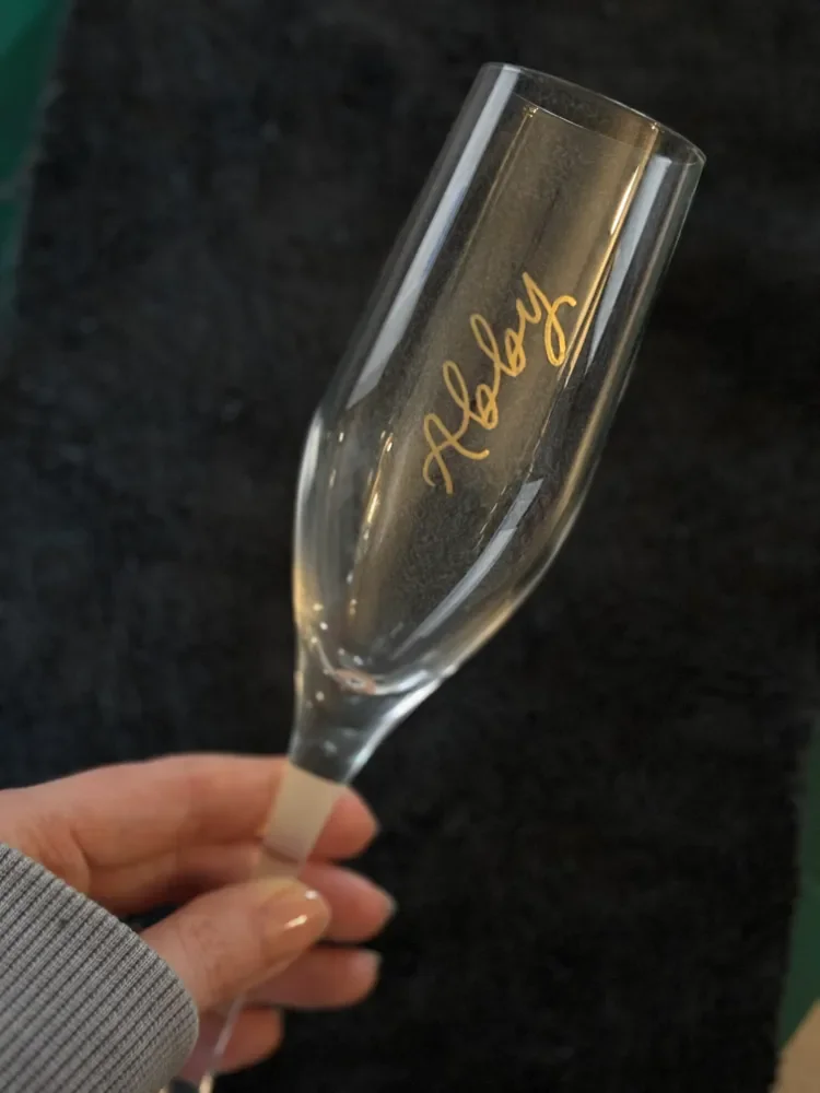 Abby inscribed in calligraphy script with gold metallic pen on the side of a champagne flute