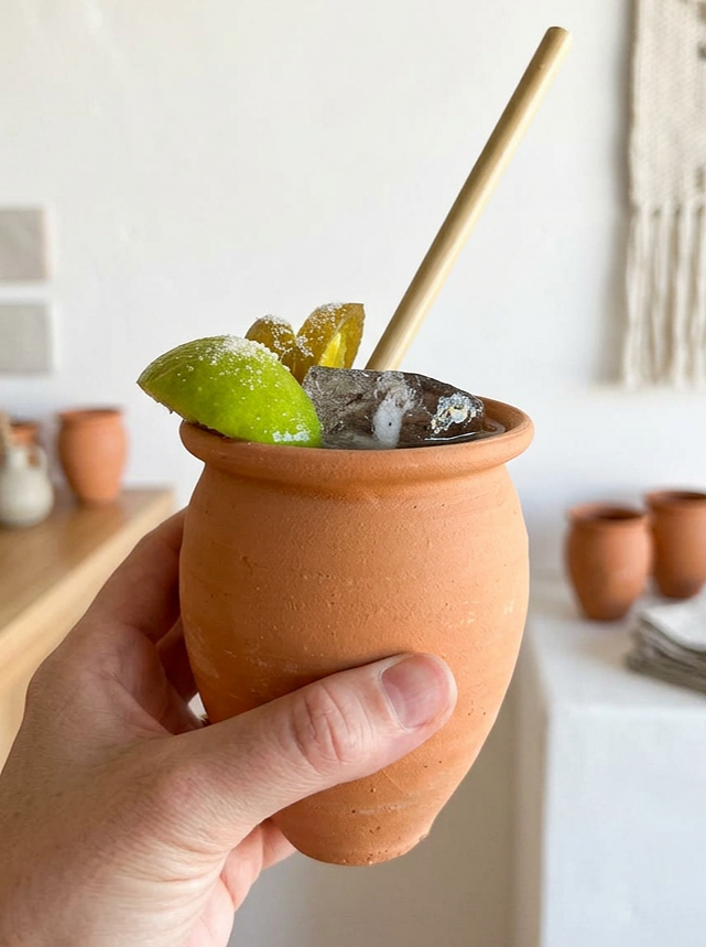 Mexican clay cantarito cocktail cups on a party table with fresh limes, ready for a fiesta-style get-together