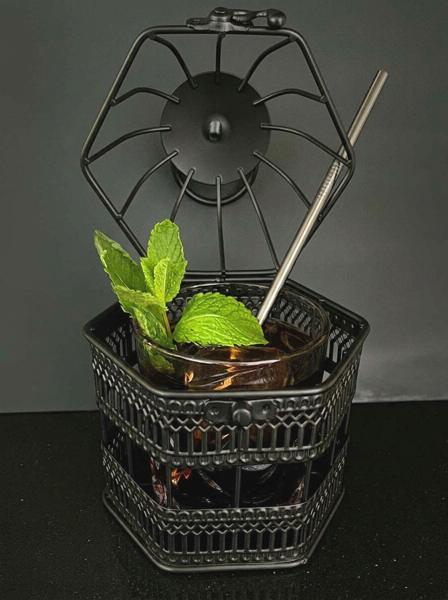 Black mini bird cage with cut glass cocktail glass inside with top of the cage open and drink inside