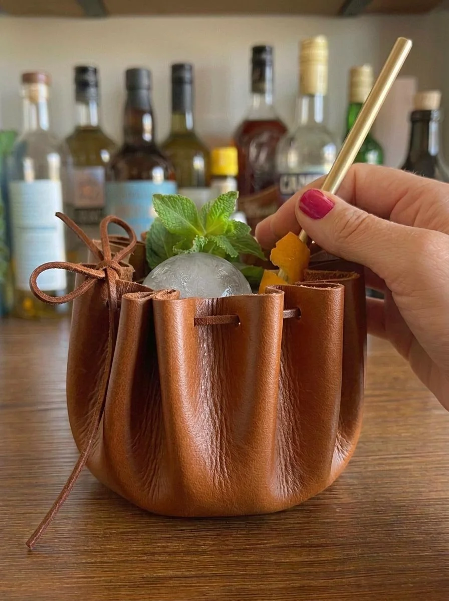 TAN LEATHER OUTLAWS POUCH WITH GLASS WITH HAND.jpg