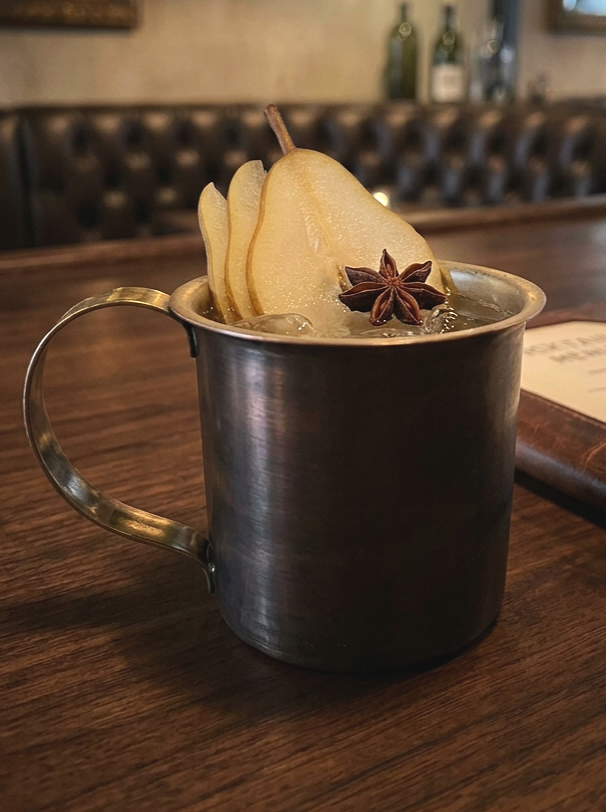 Blackend copper mule cocktail mug with pear and star inise garnish in a speak easy style bar top